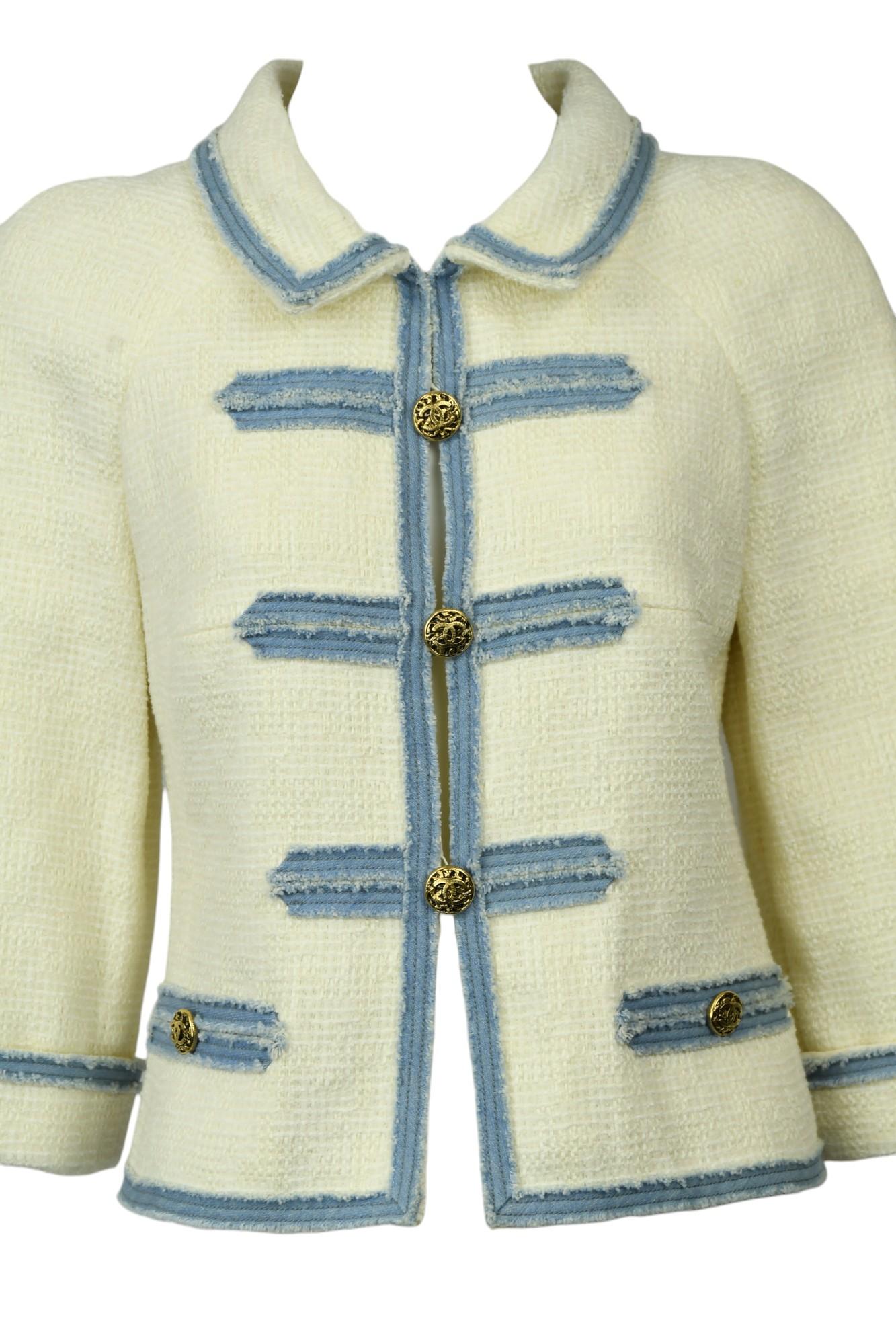 Cette veste courte Chanel est l'expression intemporelle de l'élégance classique de la marque.  Confectionné en France à partir d'un luxueux tweed ivoire, il est orné d'une bordure frangée façon denim bleu poudre et de boutons ornés en relief de