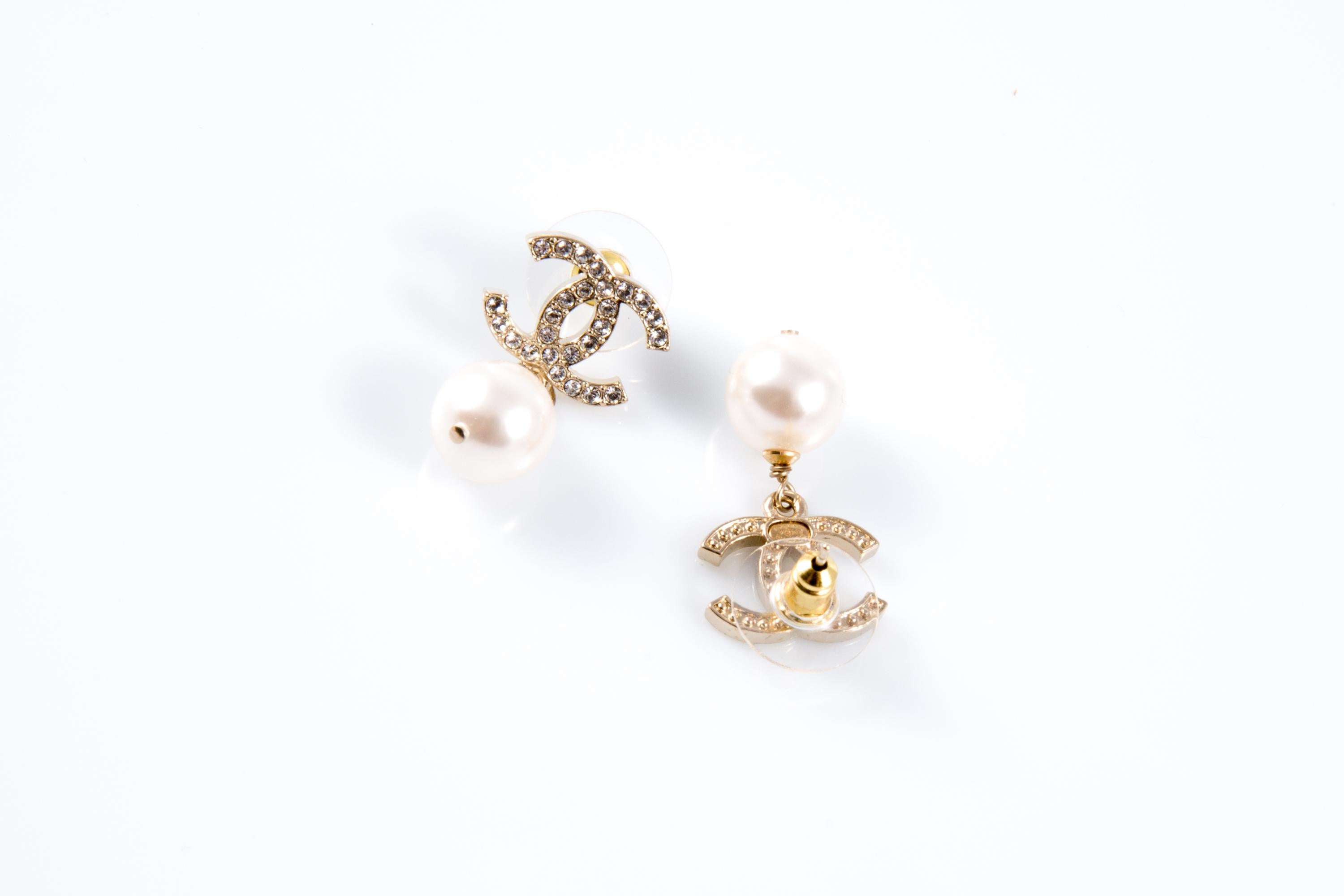 Chanel Ivory faux-pearls “CC” drop earrings featuring a gold-tone signature interlocking “CC” with crystal embellishment and  a large faux-pearl drop, a plaque pitted at back. 
They come as a pair. 
Circa 2000s  Made in France
 Length: 1in