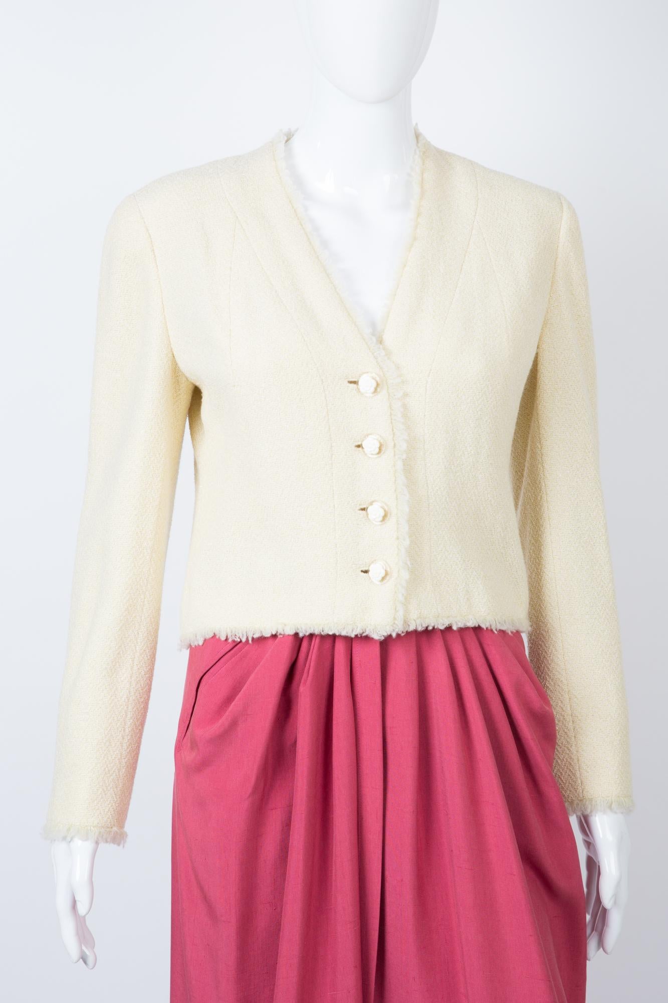 Chanel  ivory and lurex tweed wool boucle jacket 2000s Croisiere featuring a short fitted shape, a back gilet slit detail, front fancy camelias buttons, fringed edges, an ivory silk lining, and a silver hardware chain in the bottom lining.
Label