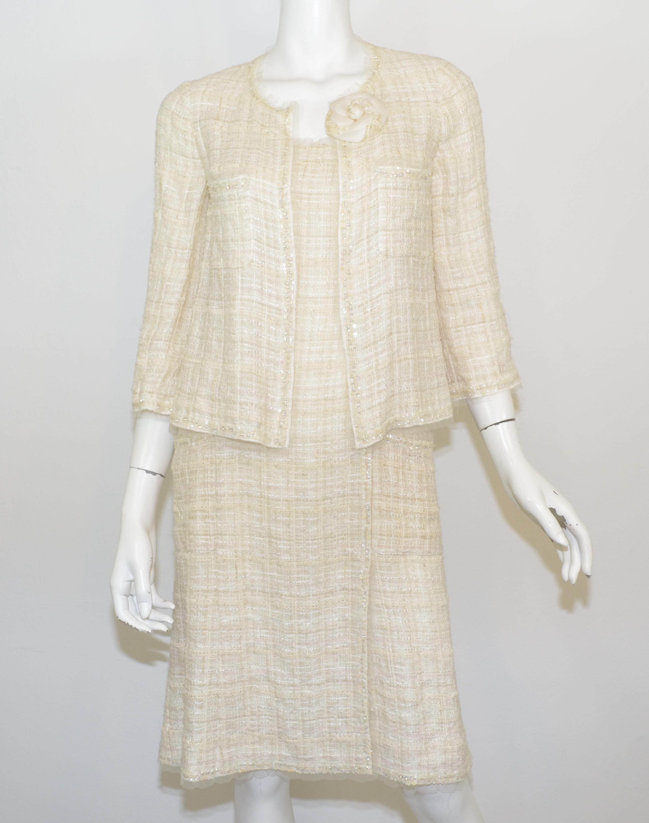 This Chanel 3-piece set includes a tweed dress, tweed jacket, and a signature Camellia brooch that is optional. Chanel set is featured in a cream, ivory tweed with a mesh trim and sequined embellishing throughout. Dress has a zipper and hook