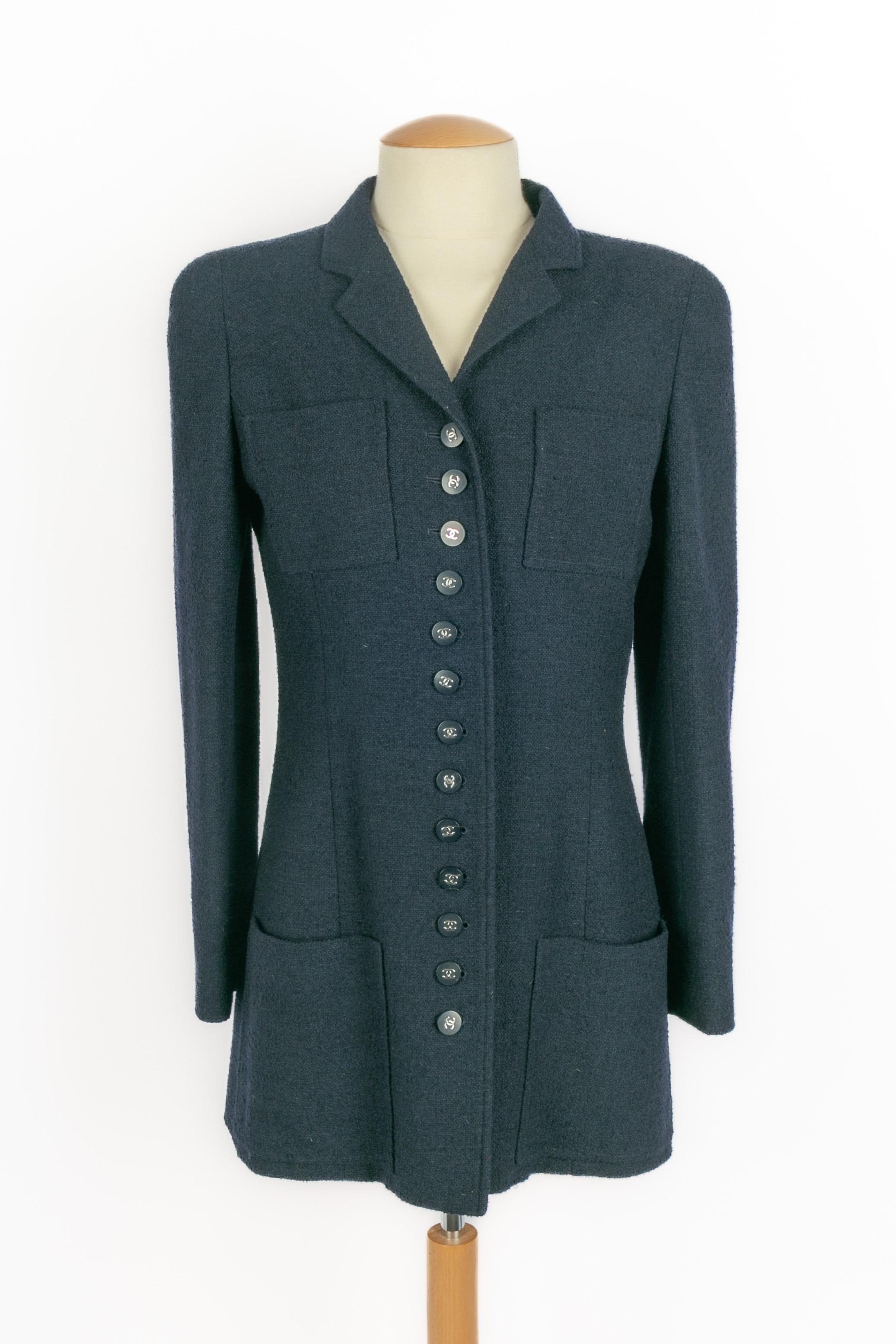Chanel - (Fabriqué en France) Veste mi-longue en laine mélangée bleu marine, boutons en résine surmontés de logos cc en métal argenté. Taille 36FR indiquée. Collectional printemps-été 1996 sous la direction artistique de Karl Lagerfeld.

Condit