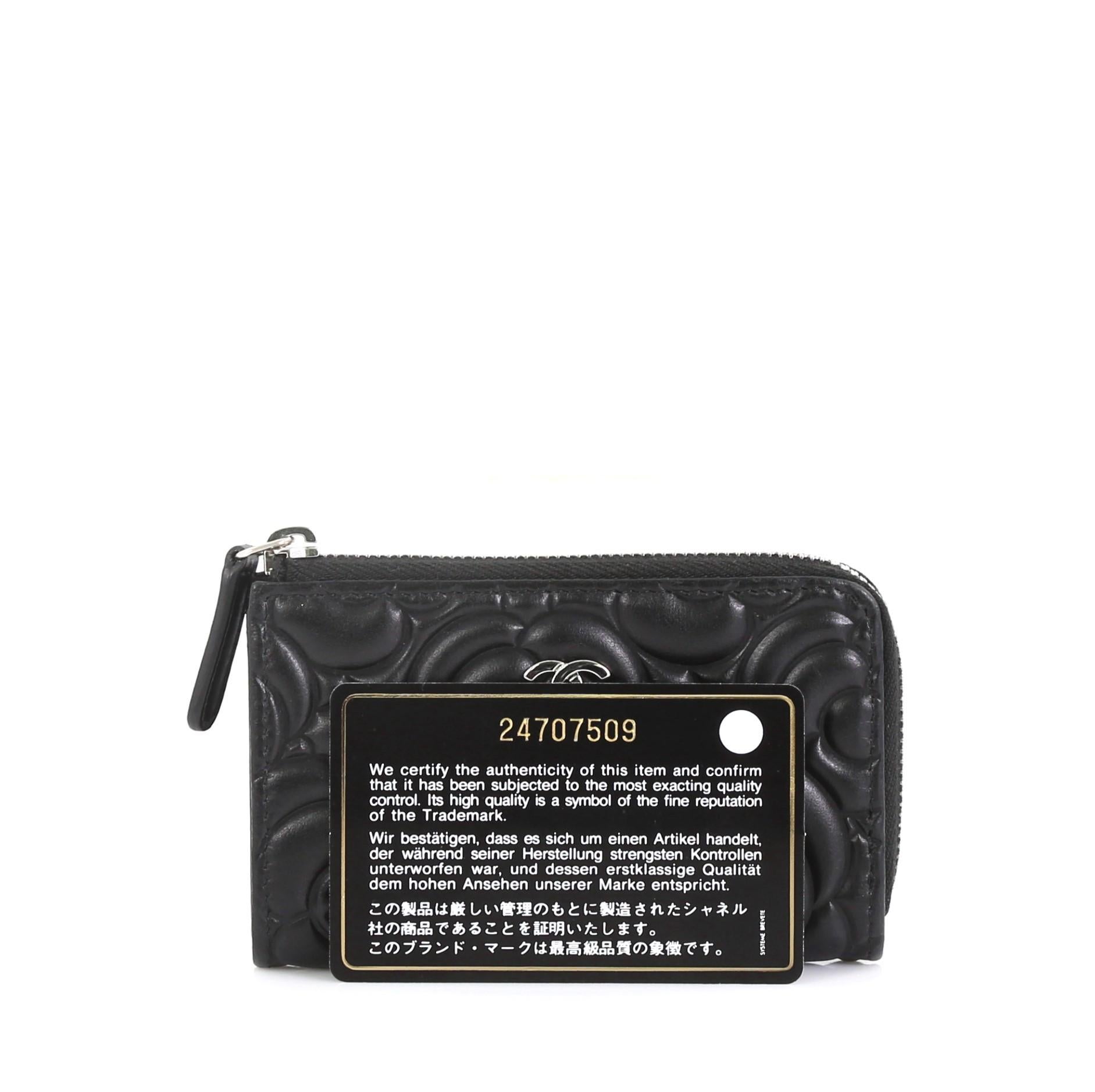 This Chanel Key Pouch Camellia Lambskin, crafted in black leather, features embossed camellia flowers with a silver Chanel CC logo and silver-tone hardware. Its zip closure opens to a black fabric interior. Hologram sticker reads: 24707509