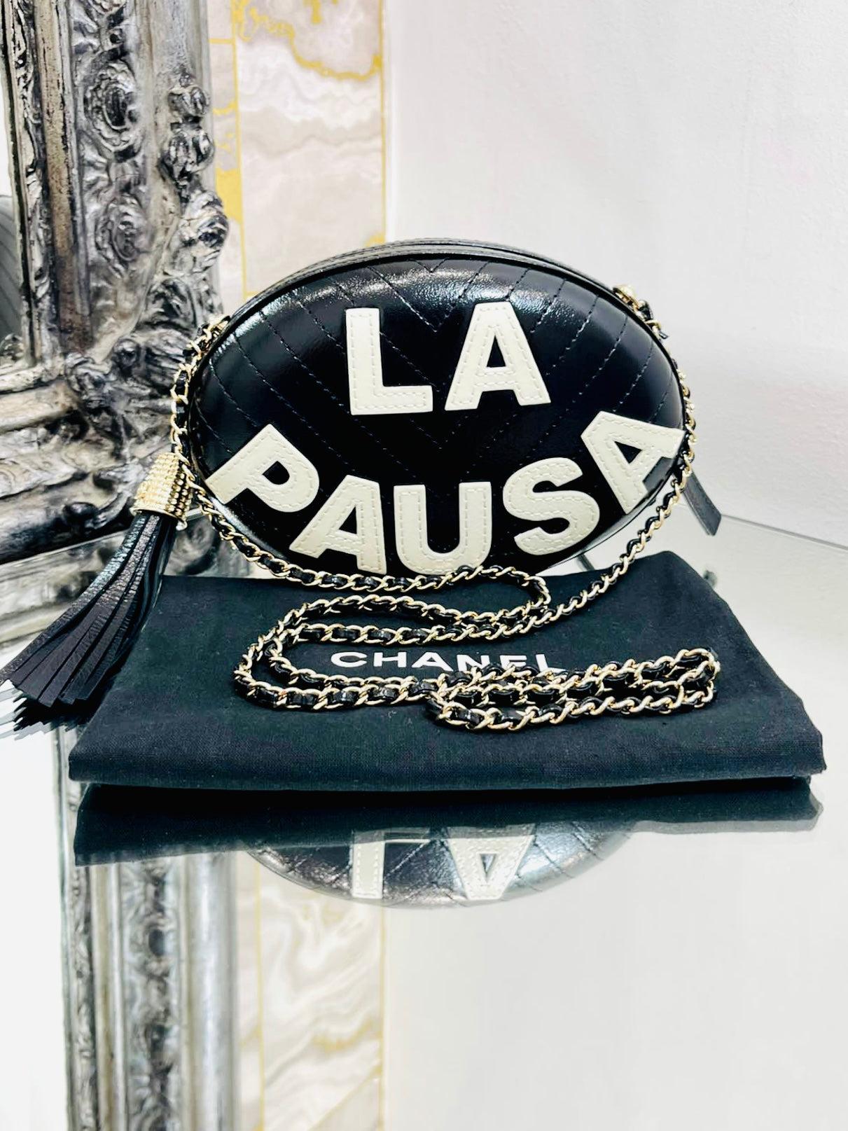 Chanel La Pausa Villa Leather Bag

Oval hard case bag in black chevron Lambskin leather with contrasting white, stitched wording 'LA PAUSA'. Gold leather and chain shoulder/crossbody strap. Gold 'CC' capped logo leather tassel. Rare find in black