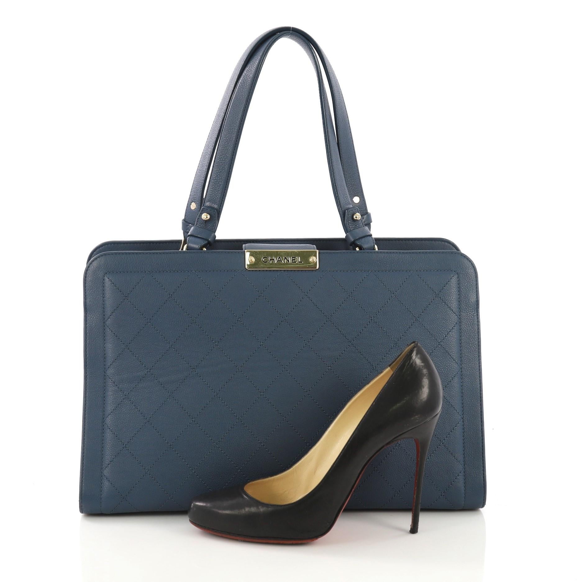 This Chanel Label Click Shopping Tote Quilted Calfskin Large, crafted in blue quilted calfskin, features dual flat leather handles and gold-tone hardware. Its magnetic snap closure opens to a beige fabric interior with center zip compartment and