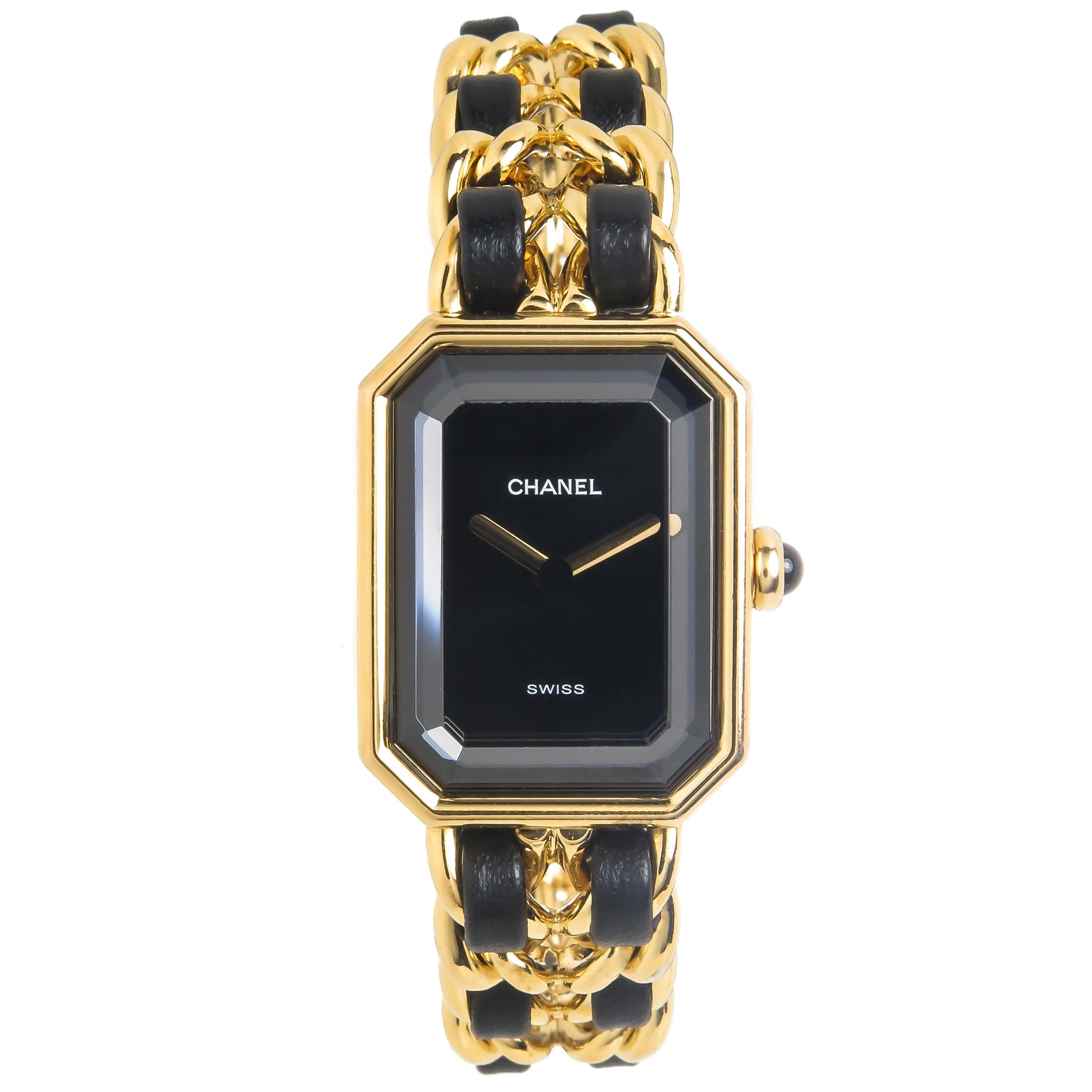 Circa 1990s Chanel Premiere collection Ladies Wrist Watch, 1 X 3/4 inch Gold Plated Case, Quartz movement , Black Dial with Gold hands a Thick faceted Crystal and a Cabochon gem set Crown.  1/2 inch wide Gold Plated link Bracelet with inter woven