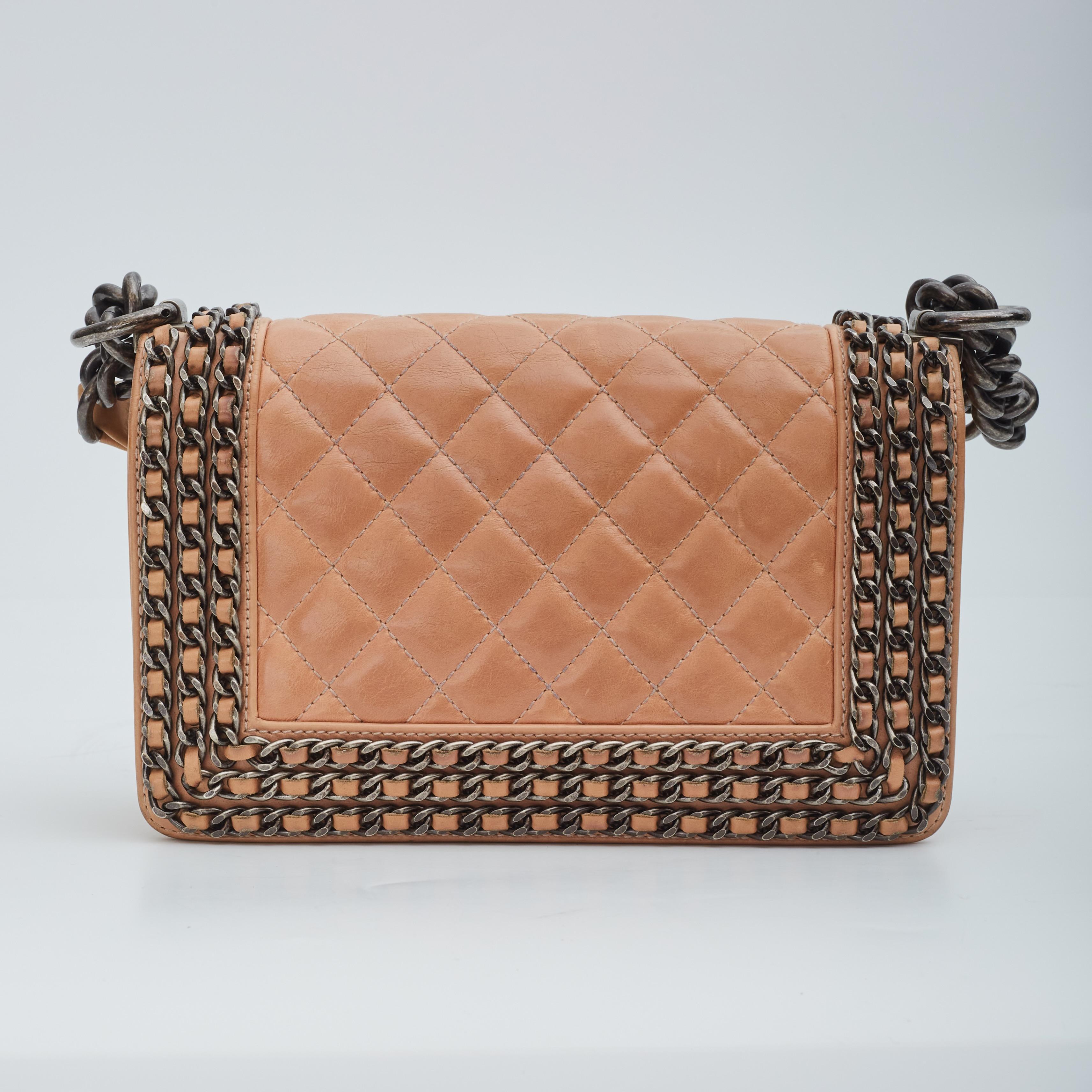 This Chanel boy bag is made of soft and supple lambskin leather in beige. The bag features ruthenium (gunmetal) hardware, chain and leather detailing around the perimeter, logo push lock closure on front flap, a should strap of a long chain attached