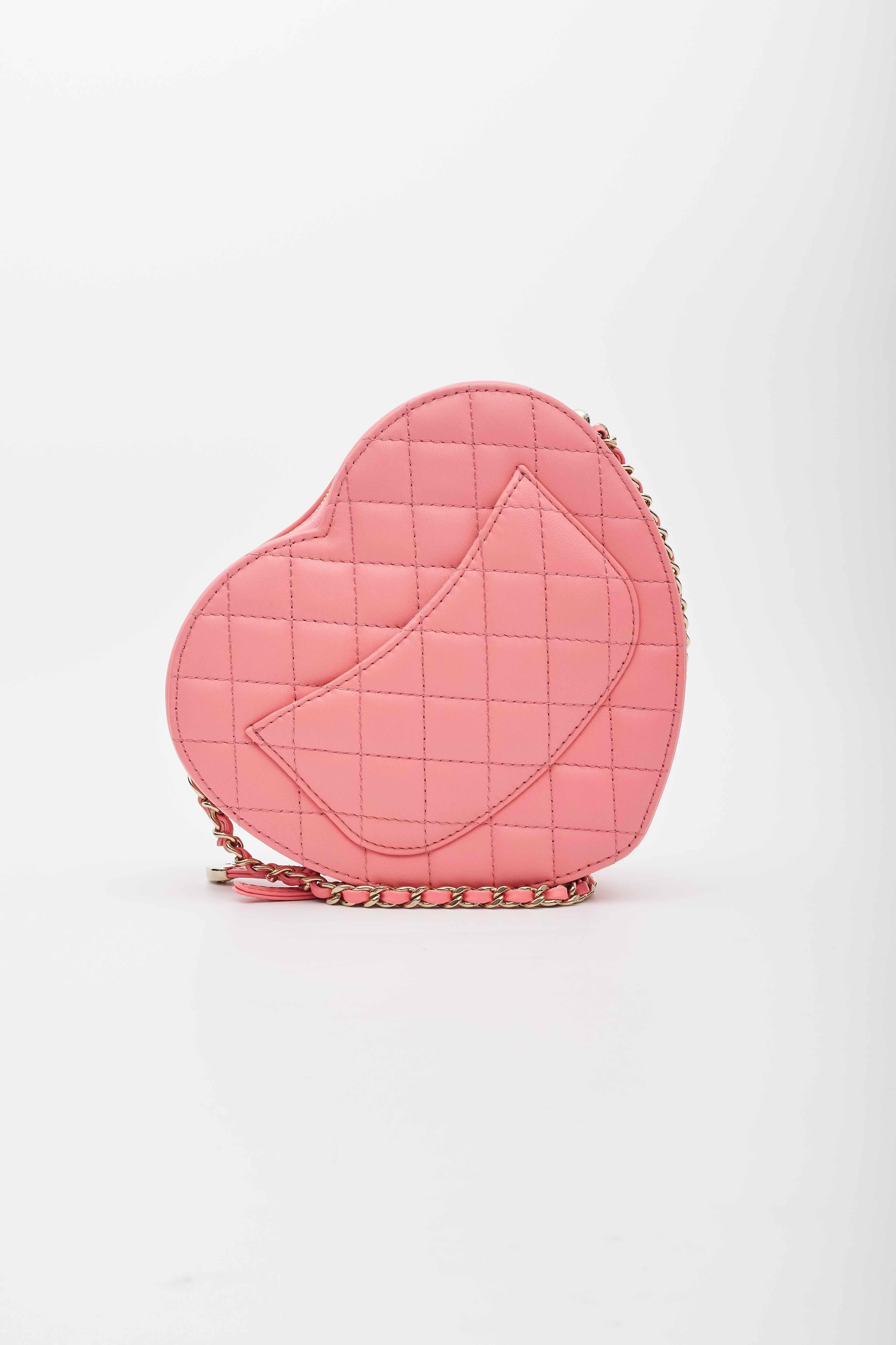 This Chanel bag is made of diamond-quilted lambskin leather in the shape of a heart. The bag features a leather-threaded light gold chain shoulder strap and a matching gold CC turn-lock on the front flap pocket. The top zipper opens to a pink fabric