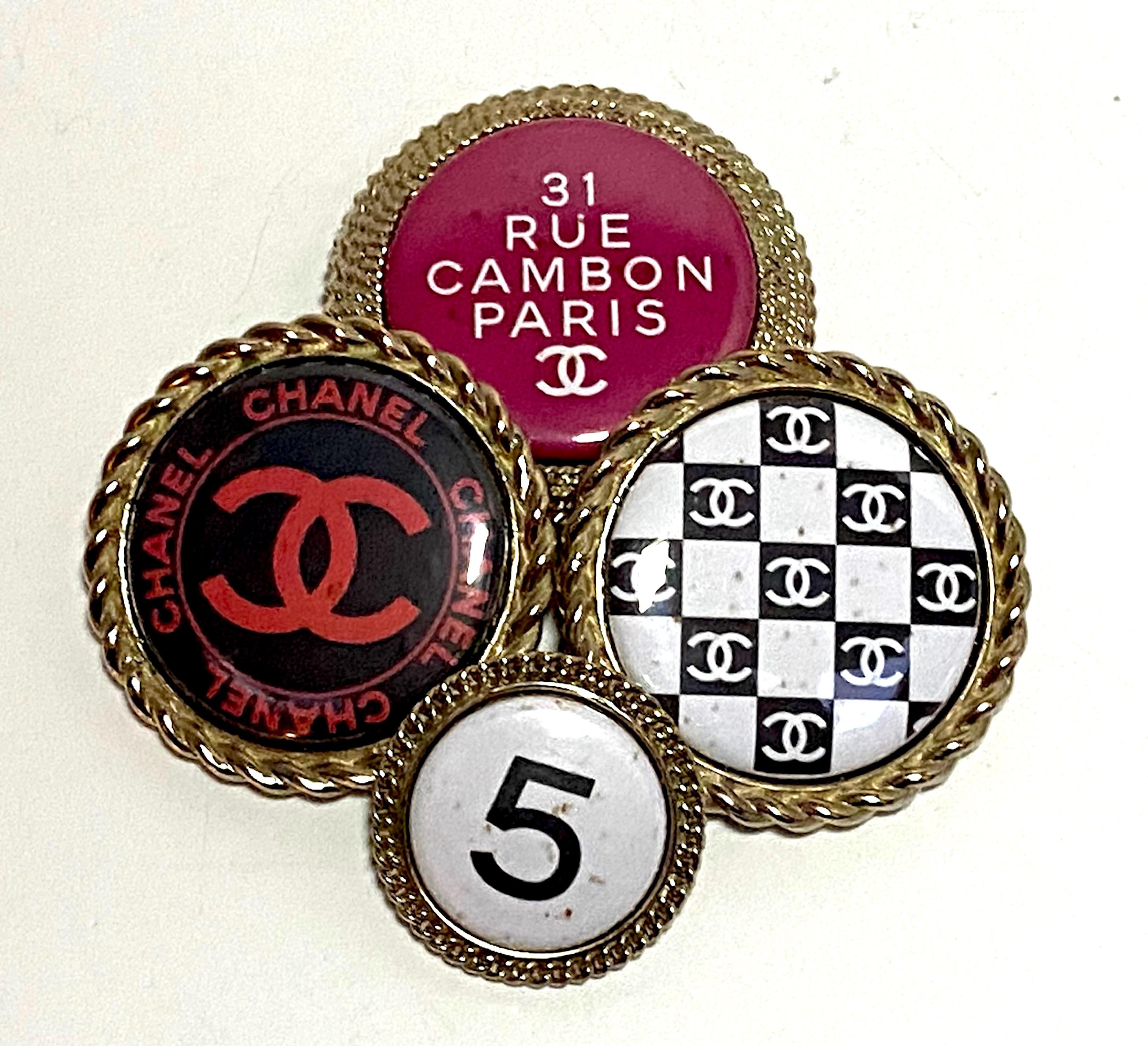 From the Spring 2008 collection is this unique fold tone Chanel brooch of four large buttons. The buttons are 1.25, 1.75 and 2 inches in diameter. Each is gold plated with a rope design border and set with a laminated graphic disk with Iconic Chanel