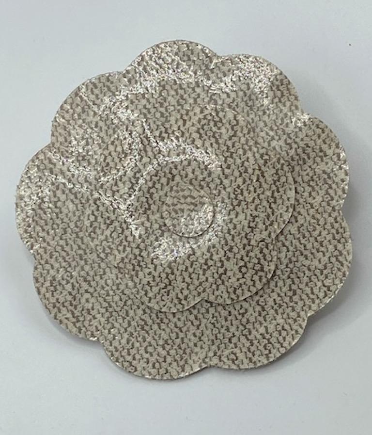 A whopping 3.5 inches in diameter is this Chanel laminated boucle/tweed fabric Camelia brooch from the 1990s. Upon close inspection one may see the creamy off white boucle thread loops woven with the taupe dark beige threads of the tweed fabric