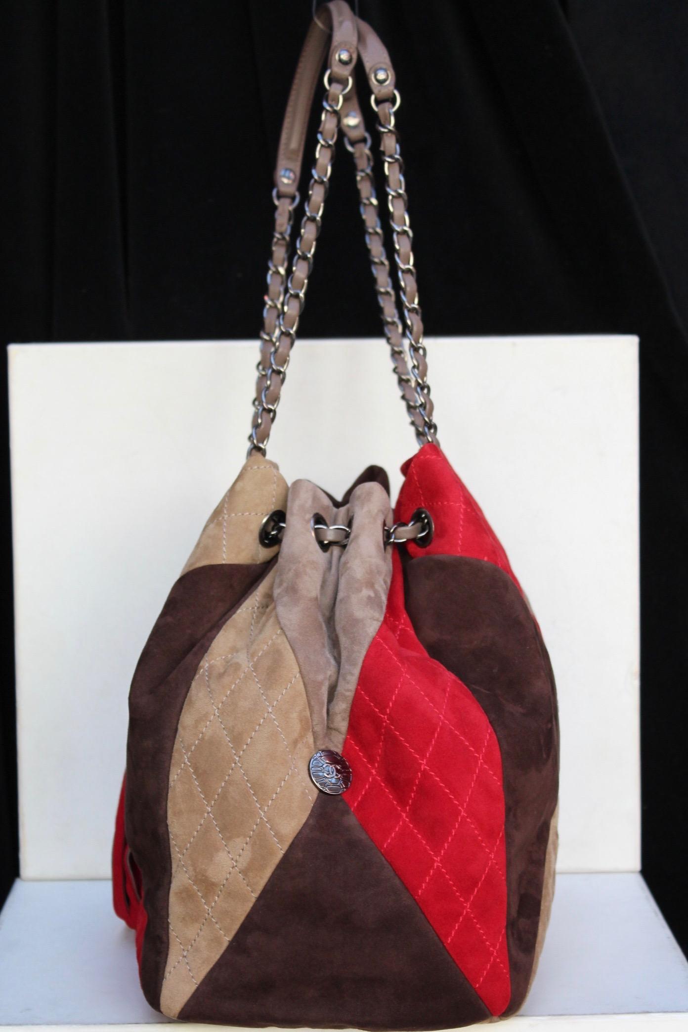 CHANEL (Made in France) Large tote bag in the shape of a purse, composed of quilted suede in a patchwork of red, brown, tan and beige colors. It features a double handle composed of silvery metal entwined with beige leather. A large red suede tassel