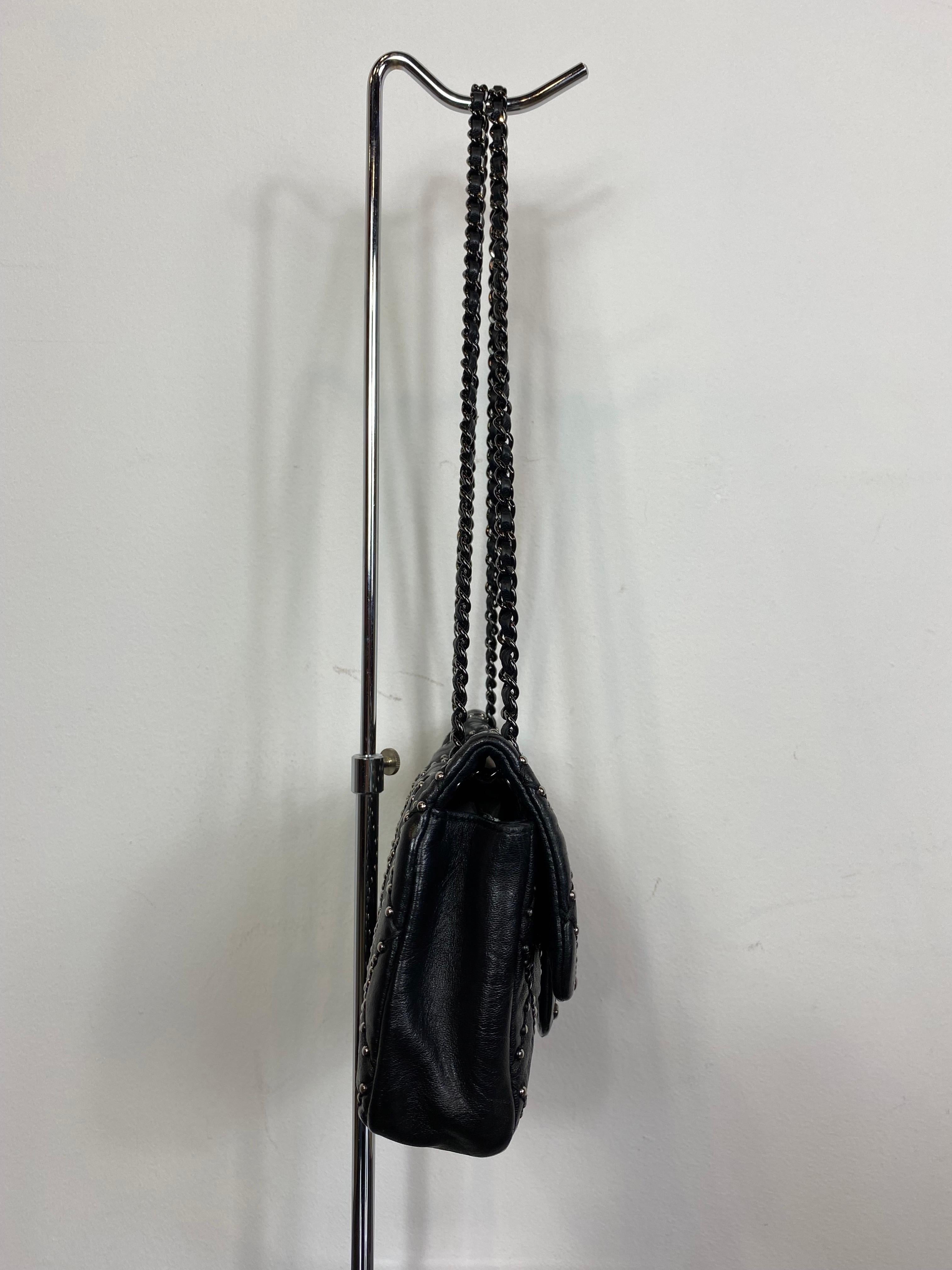 Bolso Chanel de suave piel negra con tachuelas y cadena plateada. 
Colección 2014 de Karl Lagerfeld.
En muy buen estado y con Tarjeta de autenticidad y número de serie. 
Interior de piel burdeos con bolsillo con cremallera y logotipo. 
Cierre de