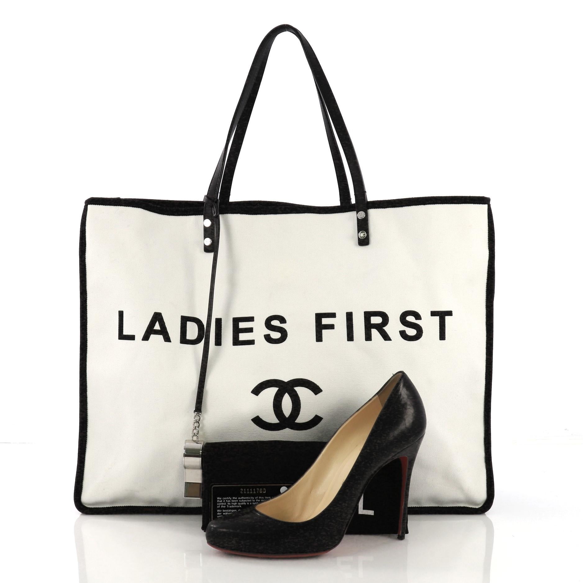 This Chanel Let's Demonstrate Tote Canvas Large, crafted from white and black canvas, features print of Ladies First and CC logo on the front, dual leather top handles, and silver-tone hardware. Its wide open top showcases a burgundy fabric interior