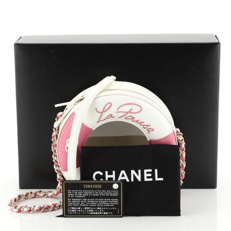 This Chanel Lifesaver Round Crossbody Bag Lambskin Small, crafted from white and pink leather, features woven-in canvas chain link strap with shoulder strap and gold-tone hardware. Its zip-around closure opens to a white leather interior. Hologram