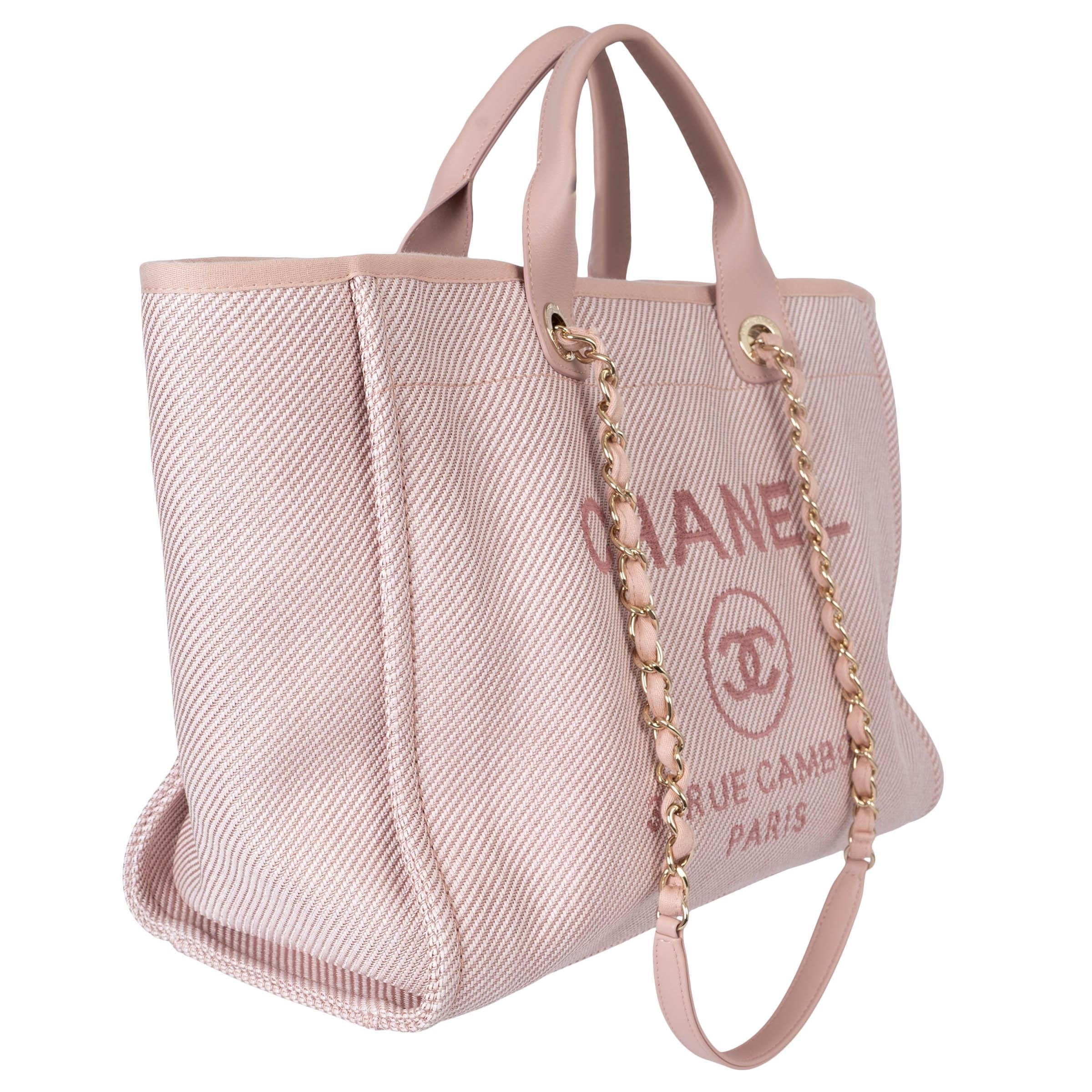 100% authentic Chanel Medium Deauville tote in light pink canvas featuring light gold-tone hardware. Opens with a magnetic button on top and is lined in light pink cotton canvas with one zipper pocket against the back and two open pockets against