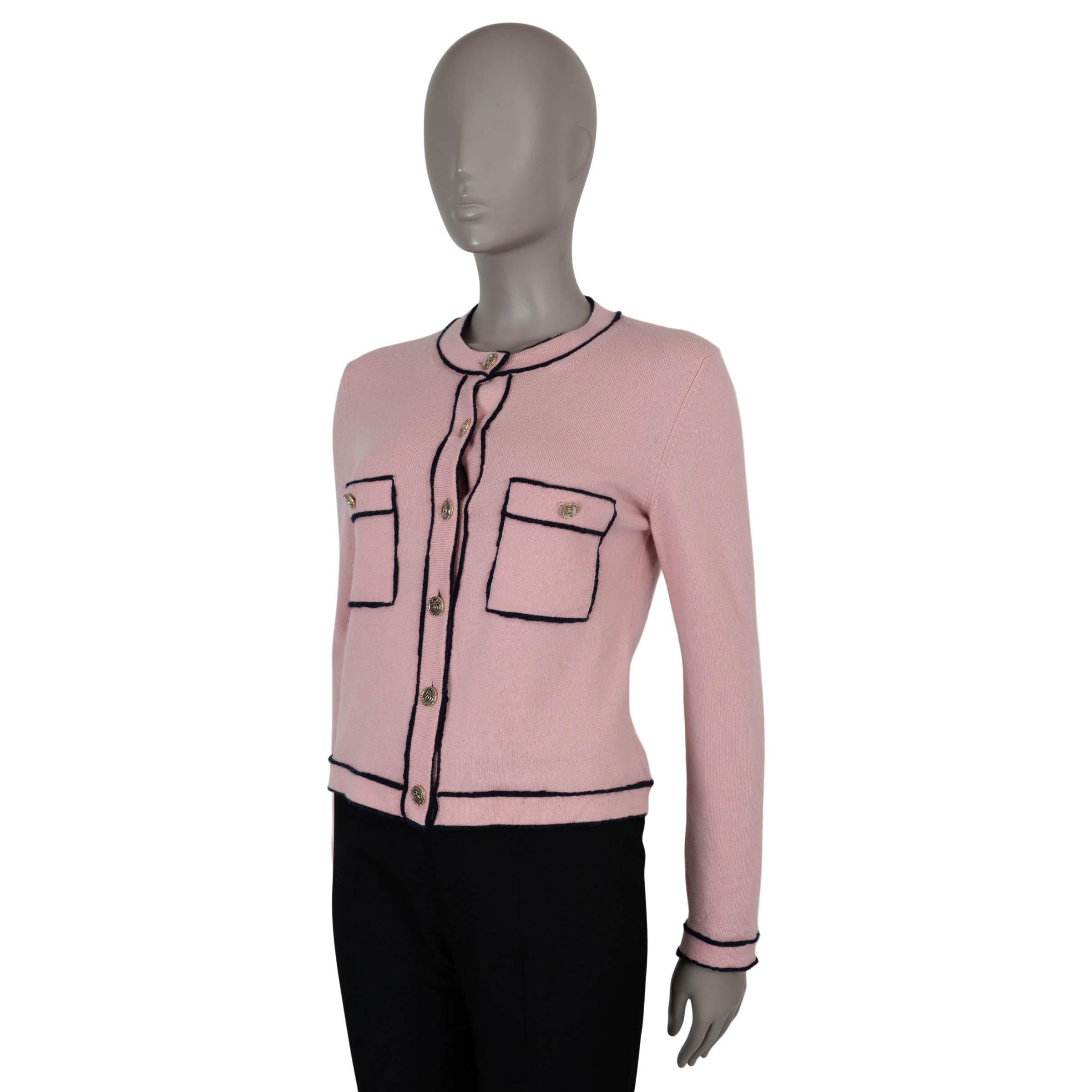 Este cárdigan Chanel 100% auténtico de cachemira rosa claro (100%) se acentúa con costuras perfiladas en azul marino en contraste para un acabado refinado. Diseñado con un corte clásico y escote redondo, tiene dos bolsillos abotonados en el pecho y