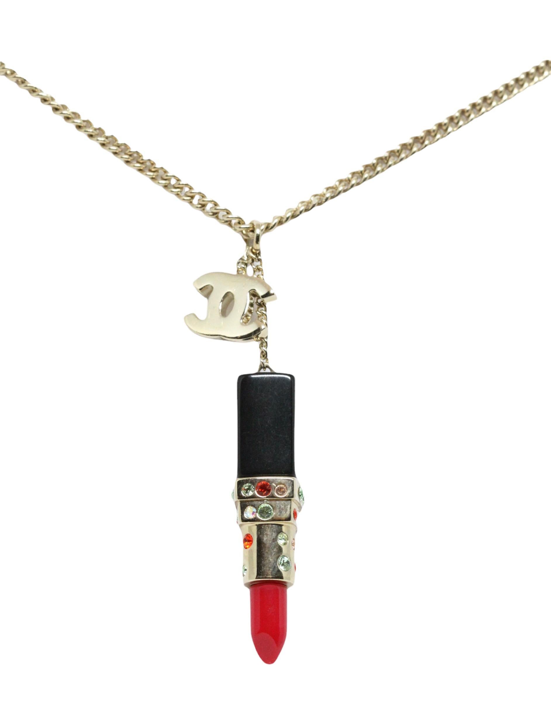 This pre-owned pendant necklace from the house of Chanel is a delicate reproduction of a lipstick.
Its gold-tone CC charm is coupled with a lipstick charm with a black base and embellished with light green and orange crystals. A shinny red lipstick