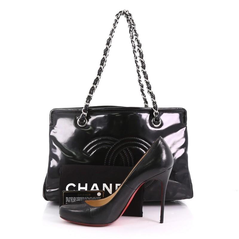 This Chanel Lipstick Tote Patent Vinyl Medium, crafted in black patent vinyl, features woven-in chain leather straps, stitched CC logo, and silver-tone hardware. It opens to a black and white fabric interior with center zip compartment and side zip