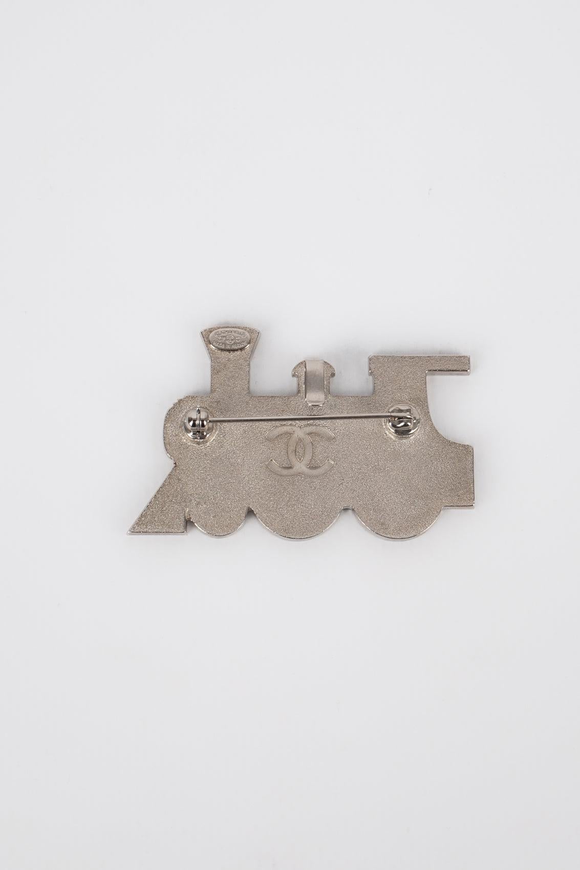 Chanel - (Made in France) Silvery metal brooch with enamel representing a locomotive. 2007 Cruise Collection.
 
 Additional information: 
 Condition: Very good condition
 Dimensions: 5.5 cm x 3.5 cm
 Period: 21st Century
 
 Seller Reference: BRB146