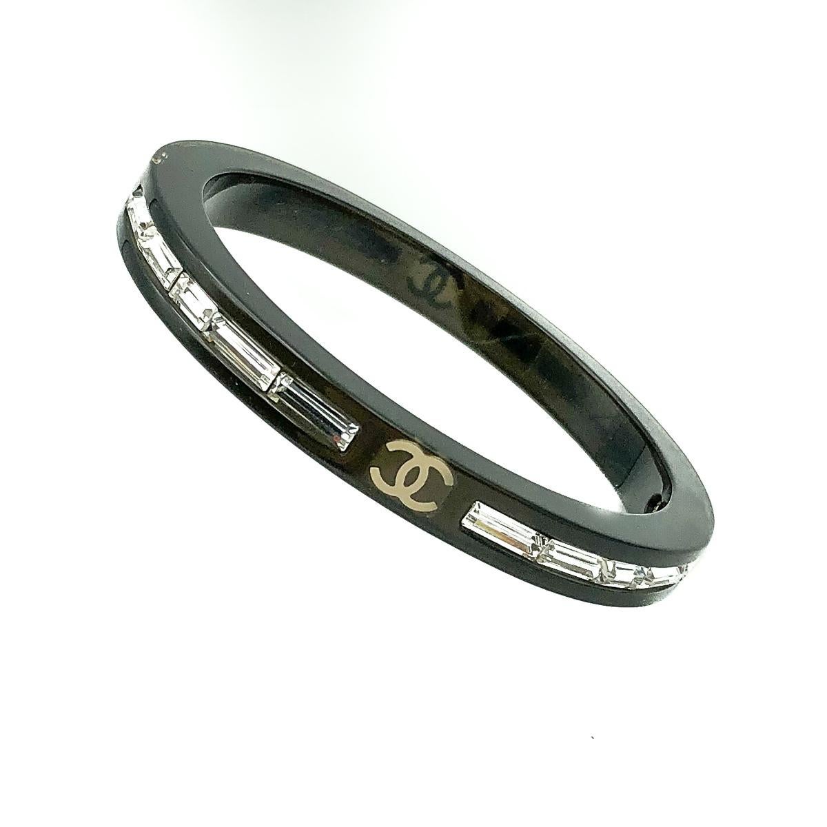 A Chanel Logo Crystal Bangle. Featuring the iconic CC logo at north, south, east and west beautifully interspersed by crystal baguette stones that glint and glisten perfectly. 
Since 1910 when Gabrielle 'Coco' Chanel opened her first boutique, , the