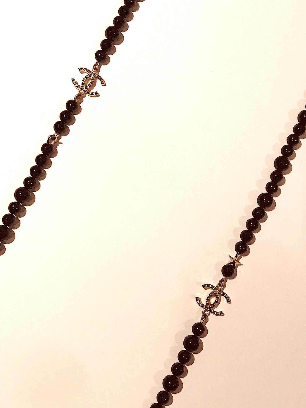 Perfect for any occasion is this long Chanel black glass bead necklace. The necklace is strung with two sizes of 7 mm and 10 mm glass beads, six small 9 mm gold stars with interlocking CC logo in center and two large 3/4 inch wide and 1/2 inch high