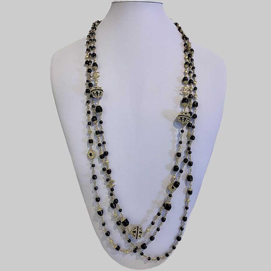 CHANEL timeless long necklace made of chiseled gilt metal in pale gold tone color. Its adorned with black molten glass pearls, a chiseled  CC charm and metal and pearl spheres (2cm each). The necklace is  112  to  120cm long plus a chain ended with