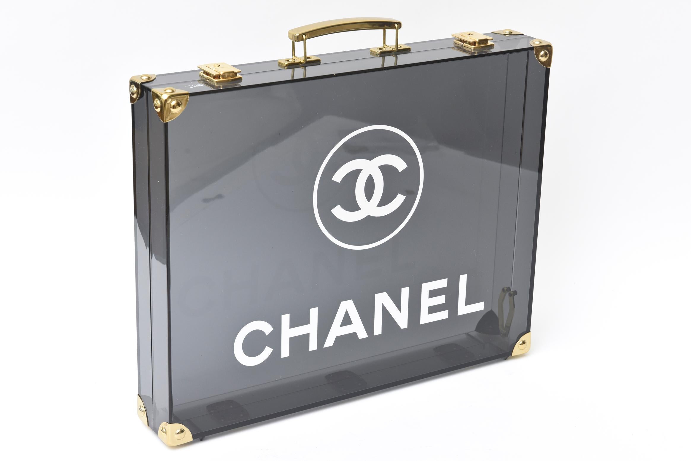 This ever so chic chanel Lucite and brass briefcase from the 1980's was made by Daby. The gray to black gradient lucite is offset against the white Chanel lettering. It was never used and has the original plastic over the case and its original box.