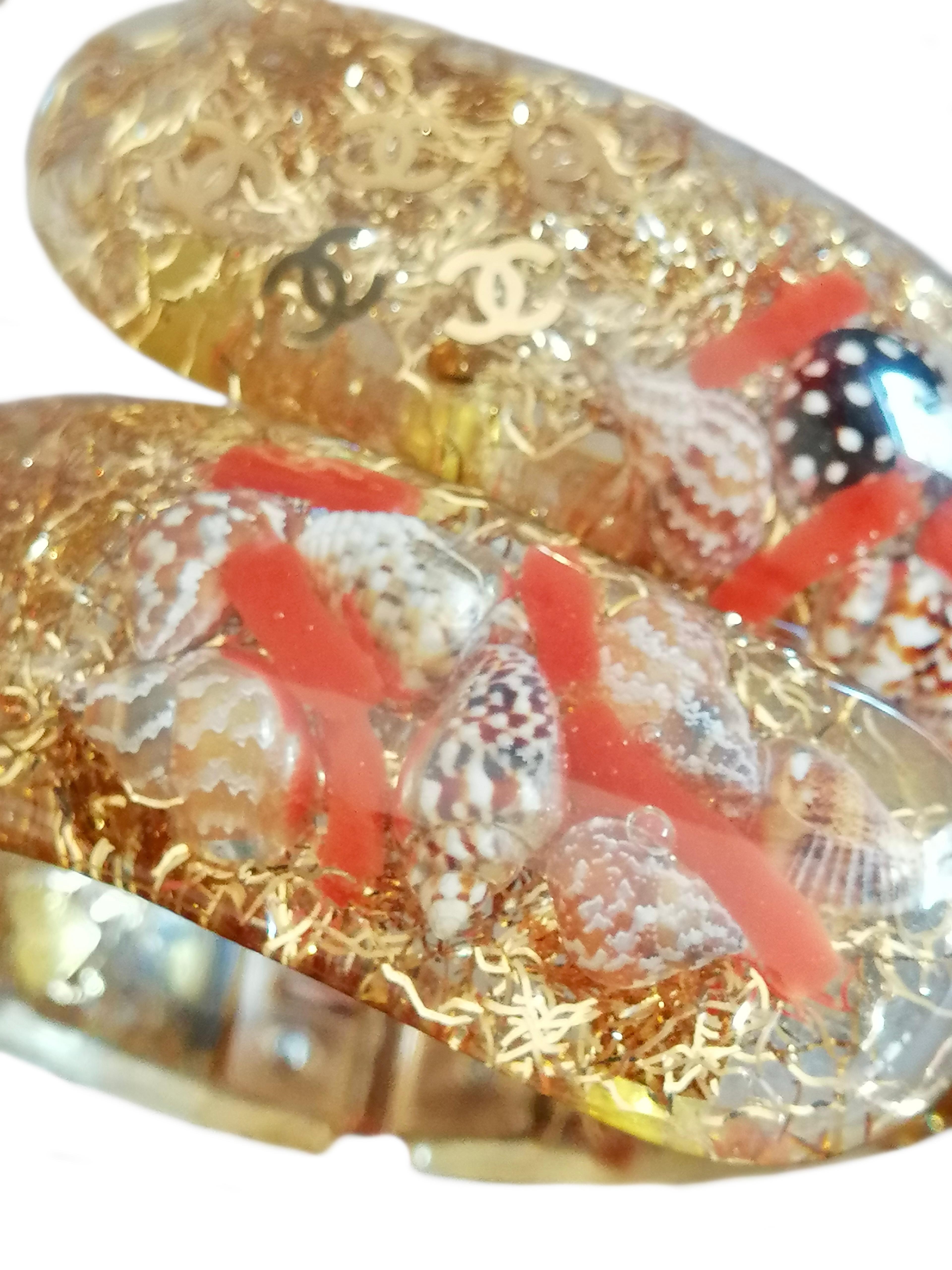 CHANEL
Pulsera brazalete con apertura de muelle en lucita transparente color champán, interior con conchas, logotipo y motas doradas.
Crucero  Colección 2005
Diámetro exterior cm. 7,5 
Diámetro interior cm. 5,5 
Altura cm. 2,5
Muy buen estado