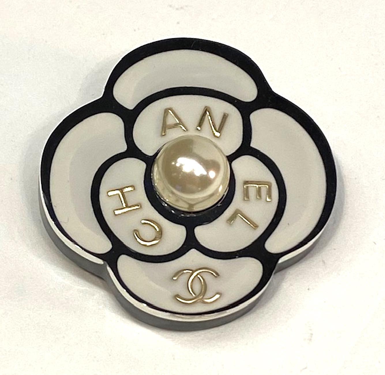 A charming Chanel camelia brooch of layered lucite with pearl. The brooch is .38 of an inch thick with the top half in clear and the bottom half in black lucite resin. Sandwiched between the two layers is the black and white image of the flower with