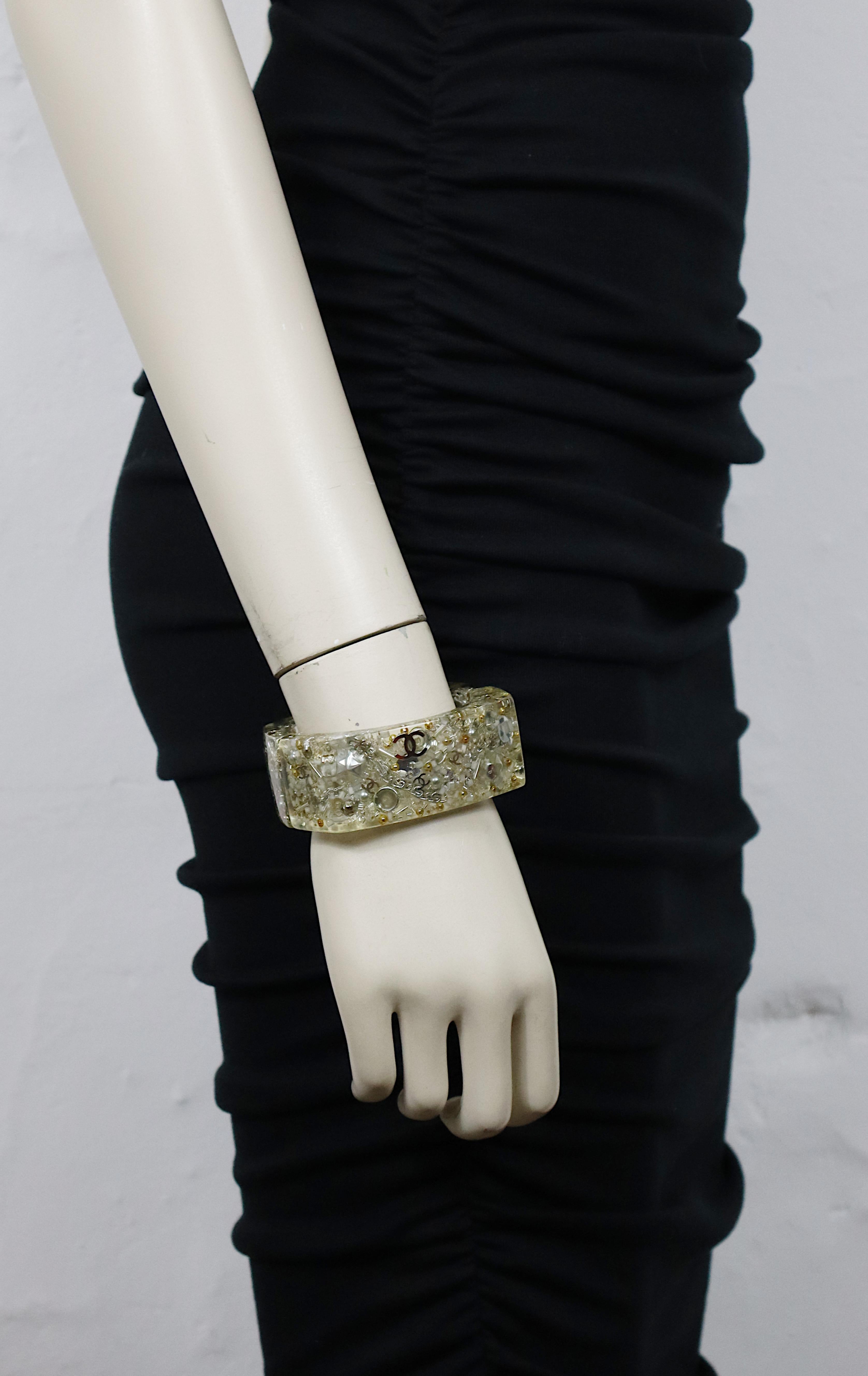 Bracelet manchette en lucite de Chanel, orné de perles et de logos CC en ton argenté.

Embossé CHANEL 13 B Made in France.

Fermeture à boucle magnétique.

Mesures indicatives : largeur intérieure max. environ 5,8 cm (2.28 inches) / hauteur