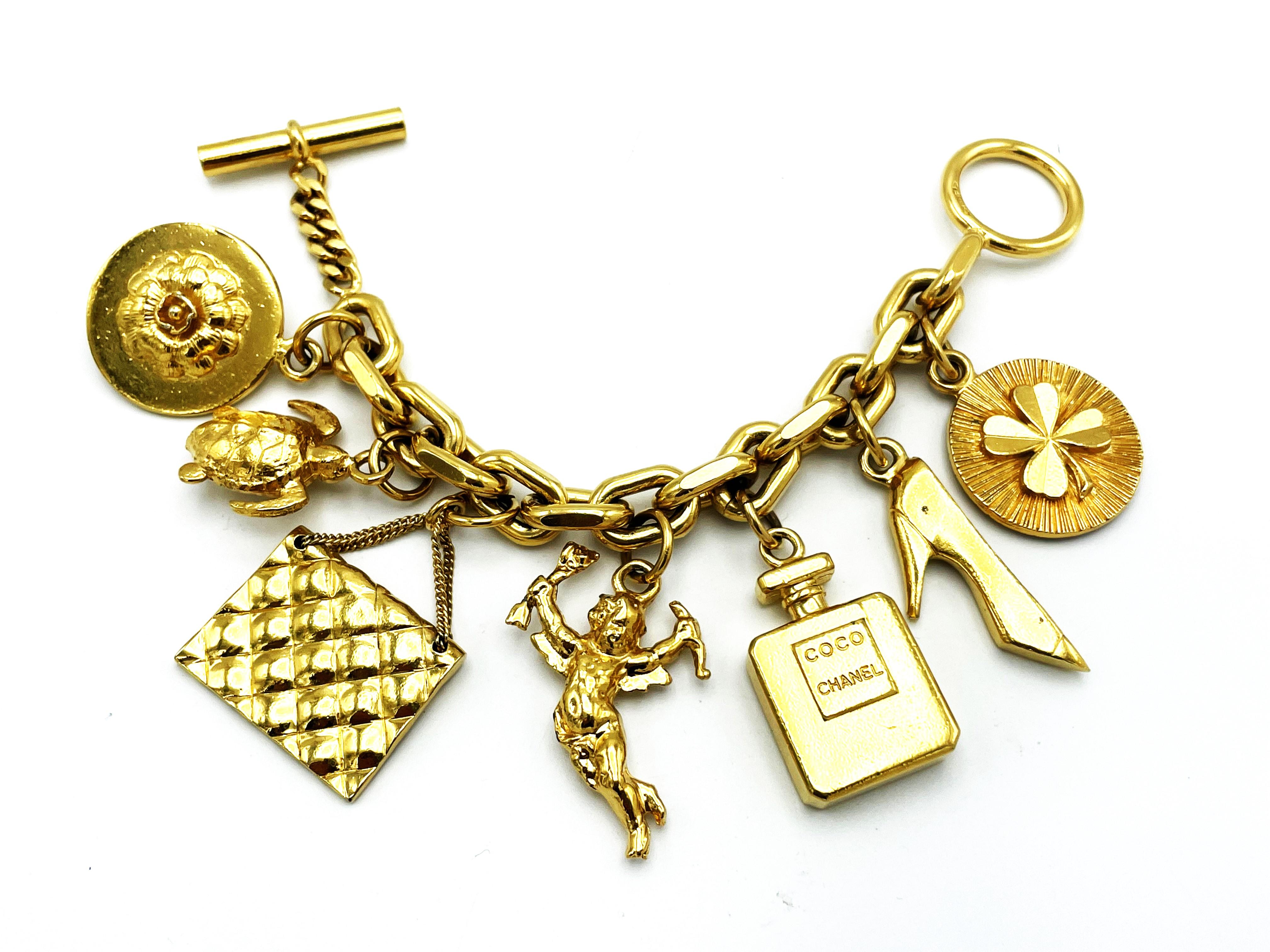 Chanels goldfarbenes Gliederarmband mit sieben ikonischen Chanel-Objekten, die an der Kette hängen: ein Kleeblatt, Absätze, eine Parfümflasche, Amor, eine gesteppte Chanel-Tasche und eine Schildkröte, eine Kamelie, die Lieblingsblume von Coco