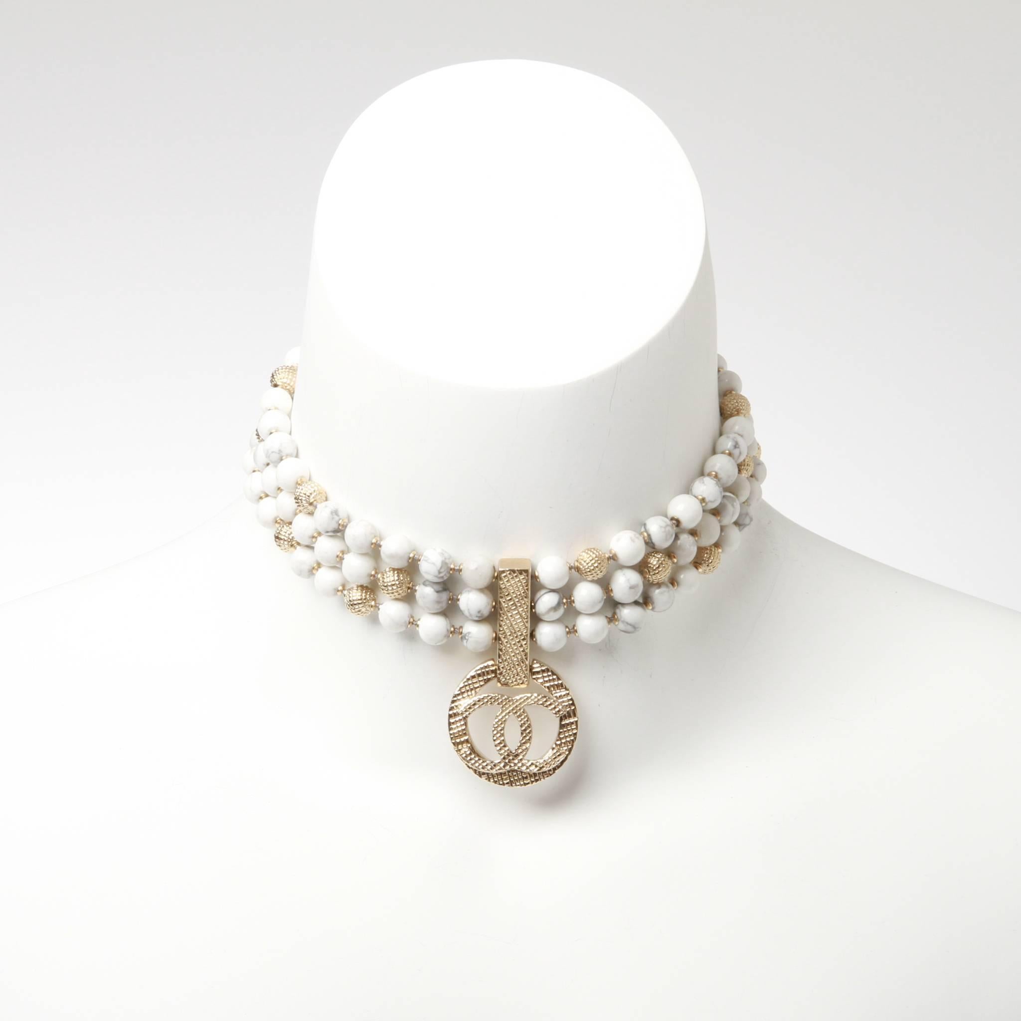 Chanel choker formed of three-strands strung with marbled and metal beads with a central CC pendant in very pale gold tone crosshatched metal. 

Stamped B16 A

Comes with box