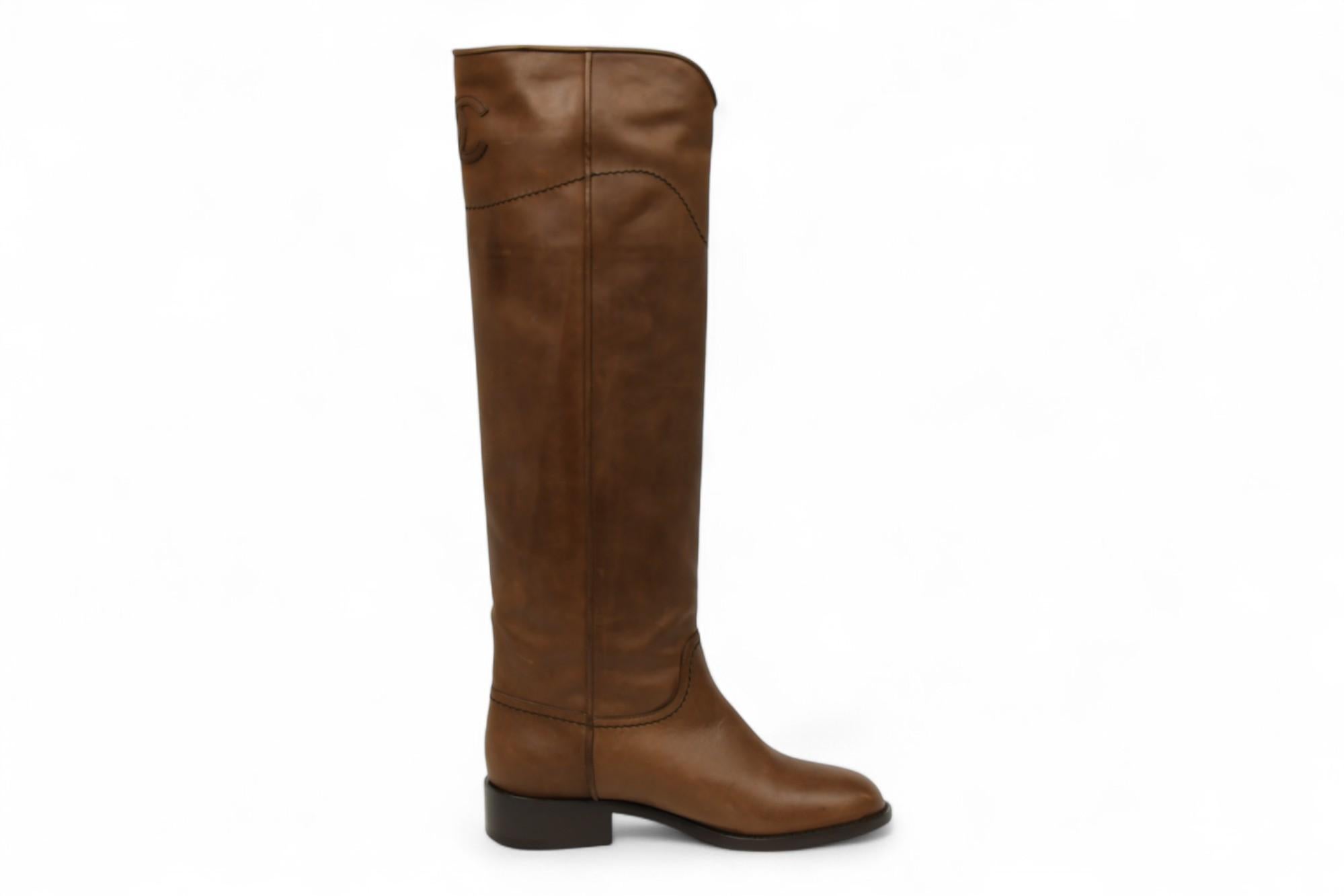 Rehaussez votre garde-robe saisonnière avec ces bottes hautes sophistiquées de Chanel en cuir marron souple. Conçues dans une silhouette de botte d'équitation emblématique, elles présentent des surpiqûres minimales et des logos CC discrètement