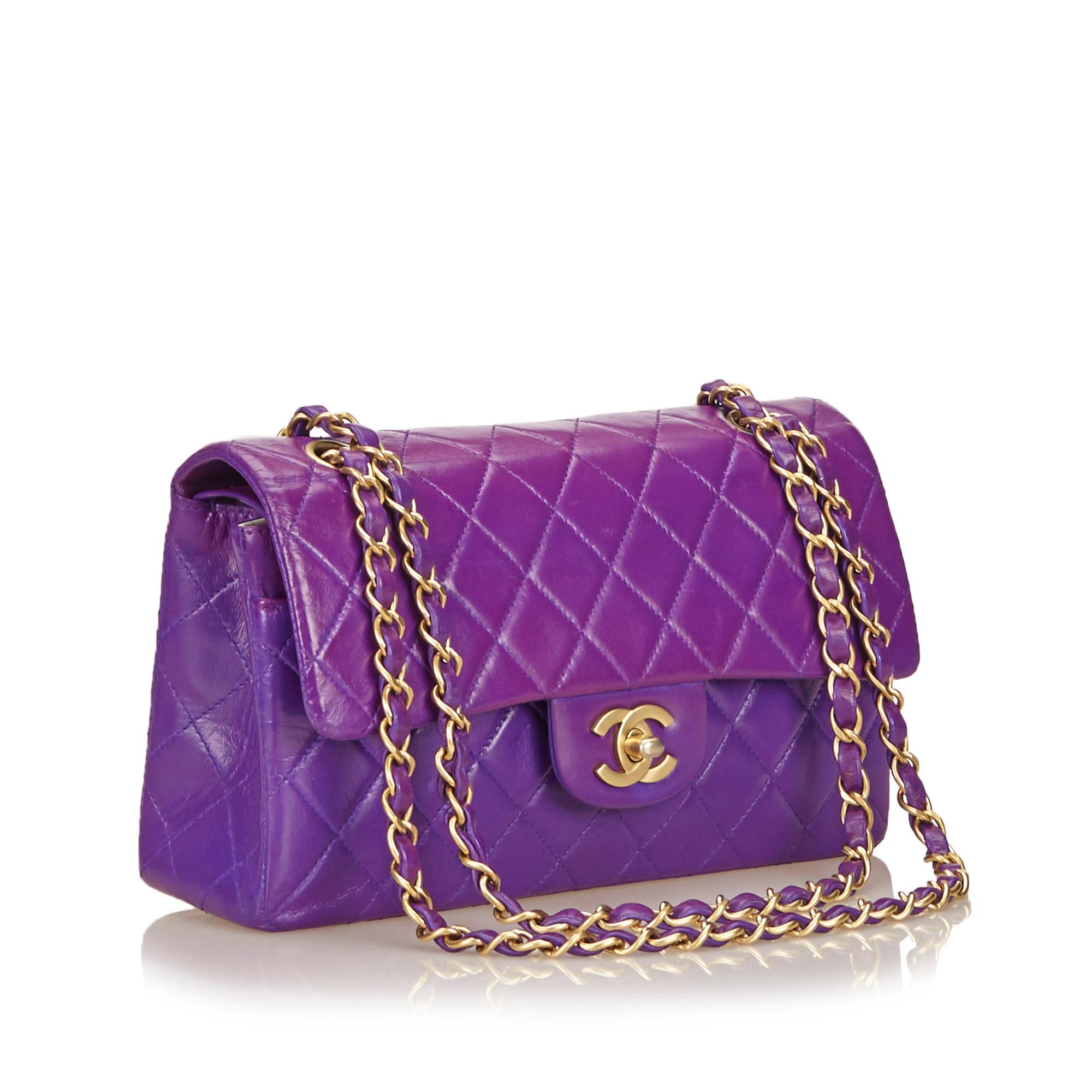 This Chanel Classic Double Flap in purple features a quilted lambskin leather body, gold-tone hardware, chain shoulder straps, an exterior back slip pocket, double front flaps with interlocking Cs and a twist-lock closure, and interior open
