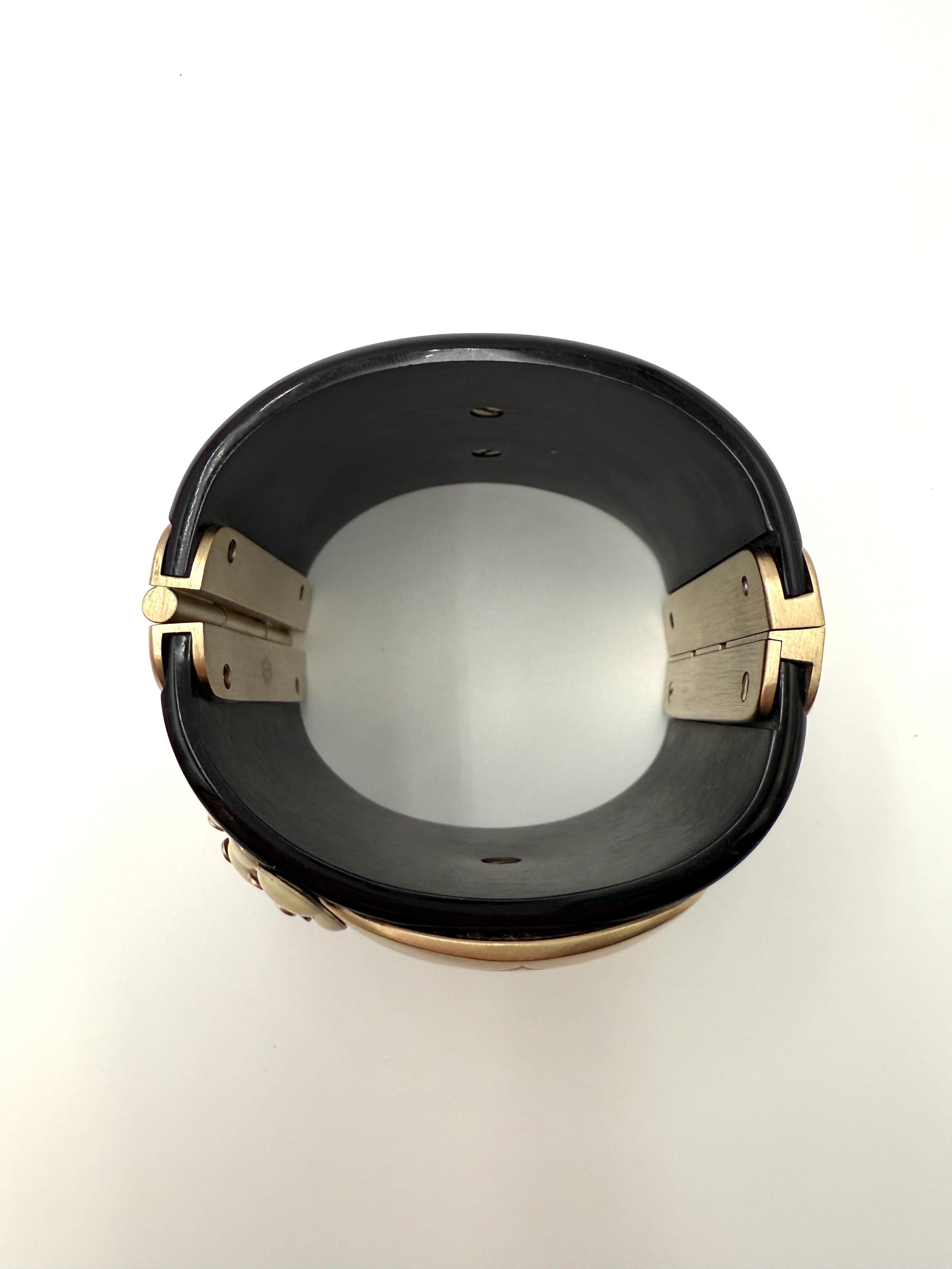 Questo rarissimo bracciale Chanel della collezione Paris-Shanghai Métiers d'Art 2010 presenta l'iconico volto della bambola Matryoshka in metallo spazzolato color oro antico, incastonato su una base di resina nera lucida. Impreziosito da delicate