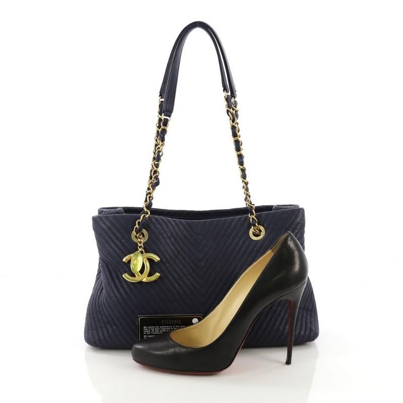 This Chanel Medallion Charm Tote Chevron Wrinkled Lambskin Medium, crafted in blue chevron wrinkled lambskin leather, features woven-in leather chain straps with leather pads, medallion charm, and gold-tone hardware. Its magnetic snap button closure
