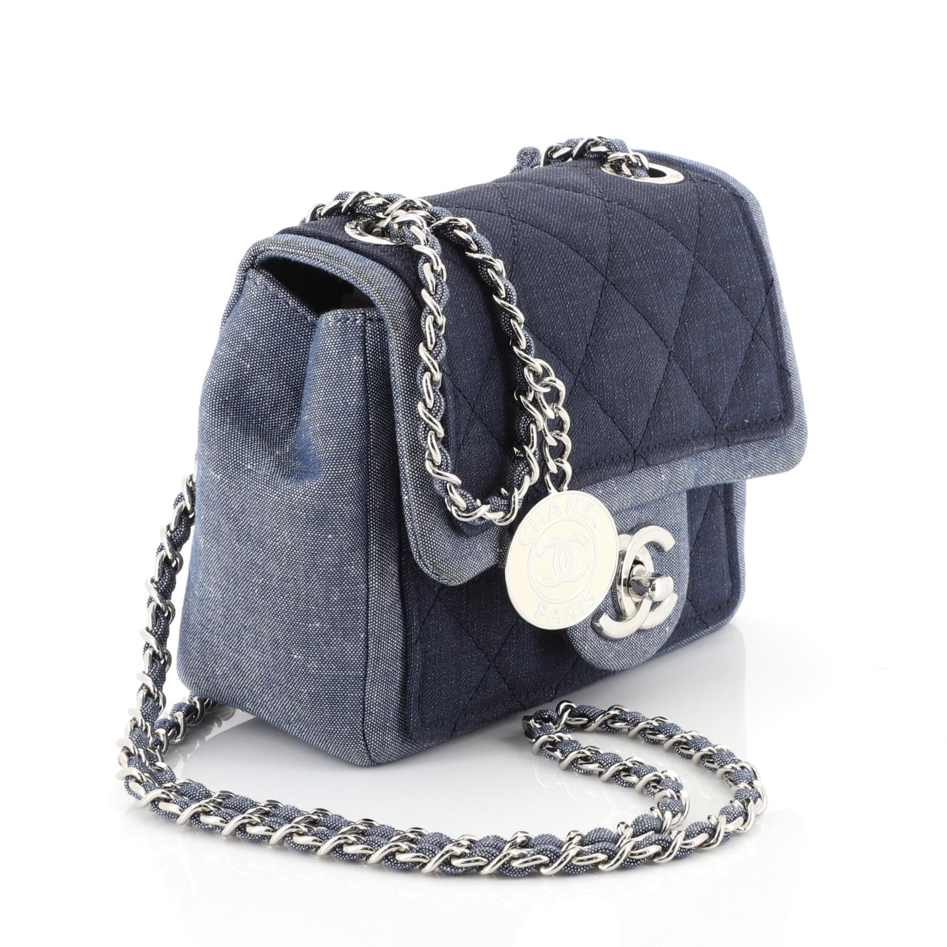 This Chanel Medallion Graphic Flap Bag Quilted Denim Mini, crafted in blue quilted denim, features woven-in denim chain strap and silver-tone hardware. Its CC turn-lock closure opens to a blue denim interior with slip pocket. Hologram sticker reads: