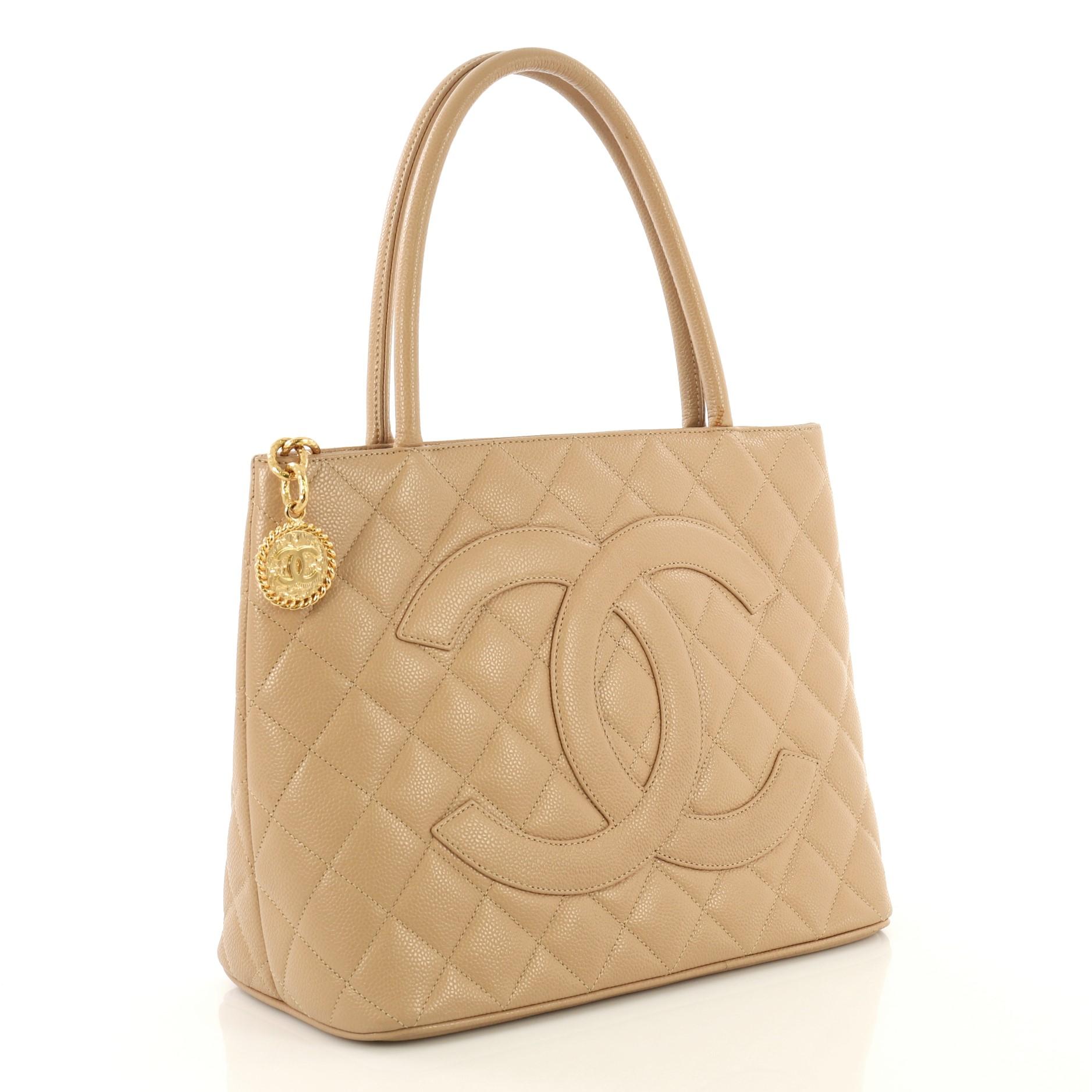 This Chanel Medallion Tote Quilted Caviar, crafted from brown quilted caviar leather, features dual rolled tall handles, oversized stitched CC logo, and gold-tone hardware. Its zip closure opens to a brown leather interior with slip and zip pockets.