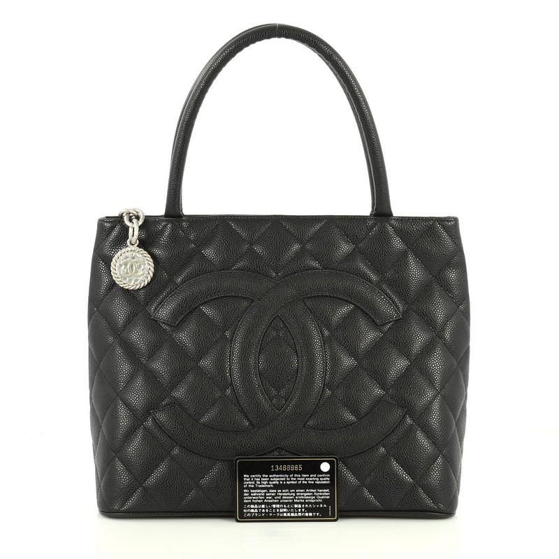 This Chanel Medallion Tote Quilted Caviar, crafted from black quilted caviar leather, features dual rolled tall handles, oversized stitched CC logo, exterior back slip pocket, and matte silver-tone hardware. Its zip closure opens to a black leather