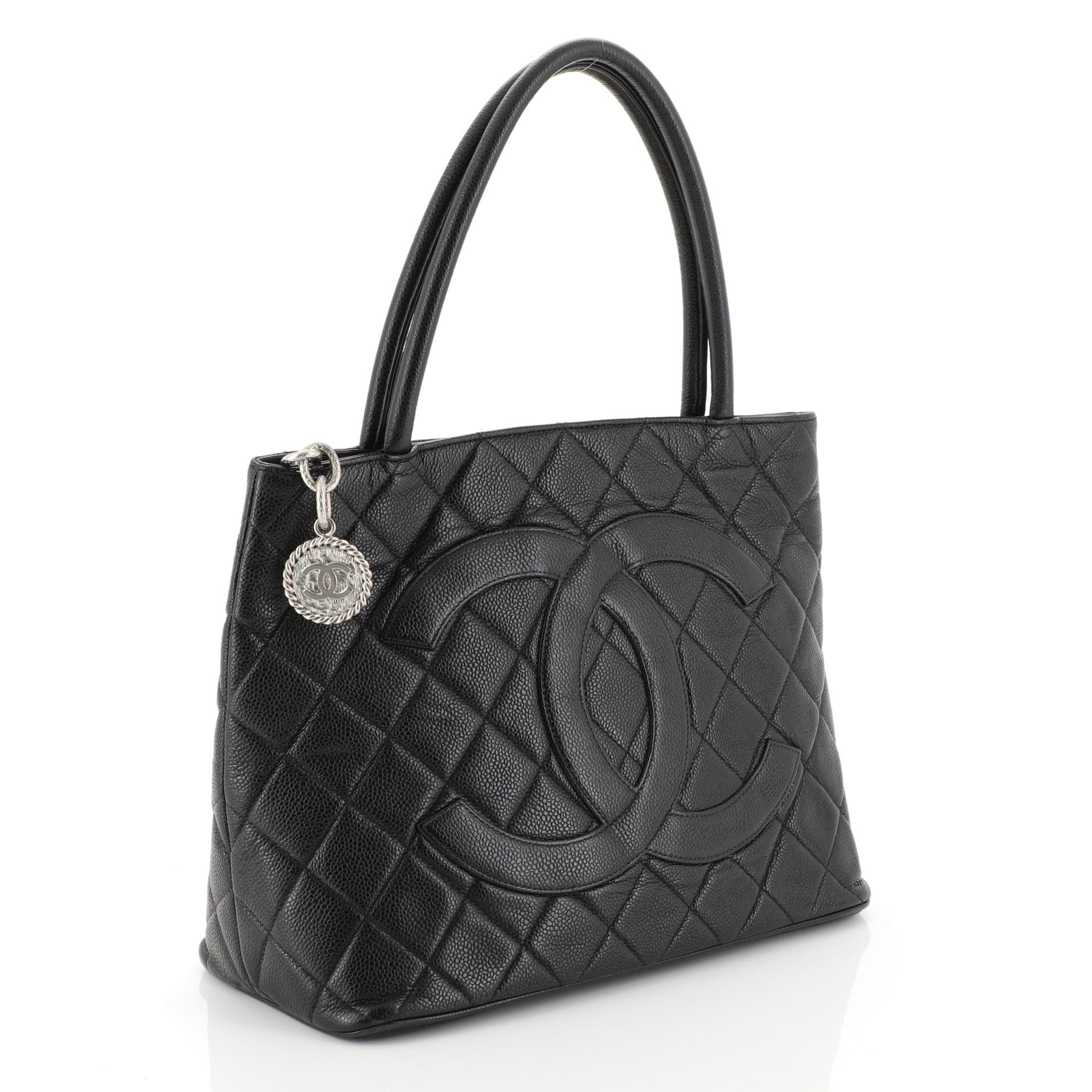 This Chanel Medallion Tote Quilted Caviar, crafted from black quilted caviar leather, features dual rolled tall handles, oversized stitched CC logo, and silver-tone hardware. Its zip closure opens to a black leather interior with slip and zip