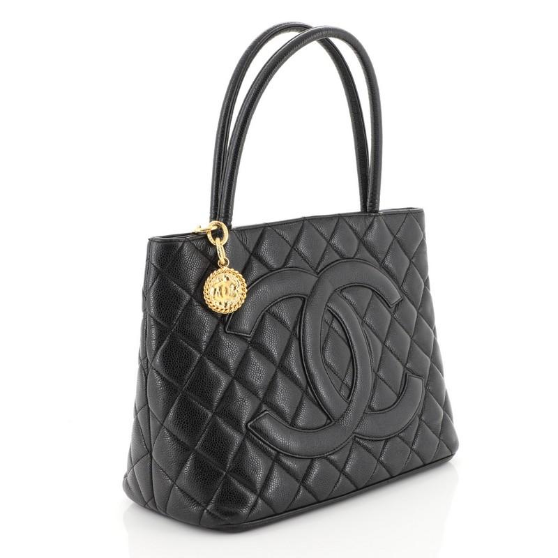 This Chanel Medallion Tote Quilted Caviar, crafted from black quilted caviar leather, features dual rolled tall handles, oversized stitched CC logo, and gold-tone hardware. Its zip closure opens to a black leather interior with slip and zip pockets.