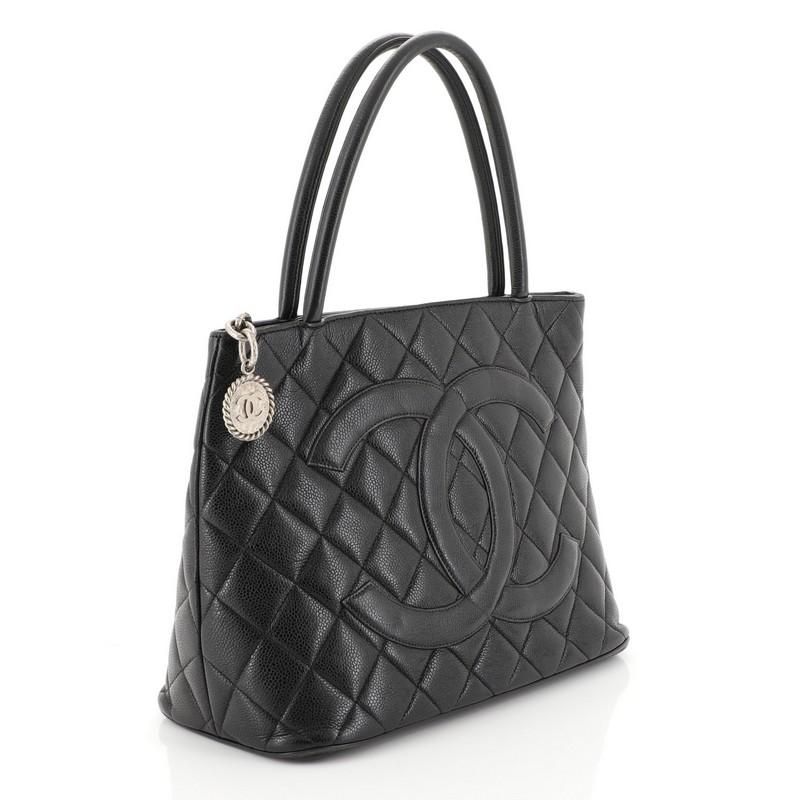 This Chanel Medallion Tote Quilted Caviar, crafted from black quilted caviar leather, features dual rolled tall handles, oversized stitched CC logo, and silver-tone hardware. Its zip closure opens to a black leather interior with slip and zip