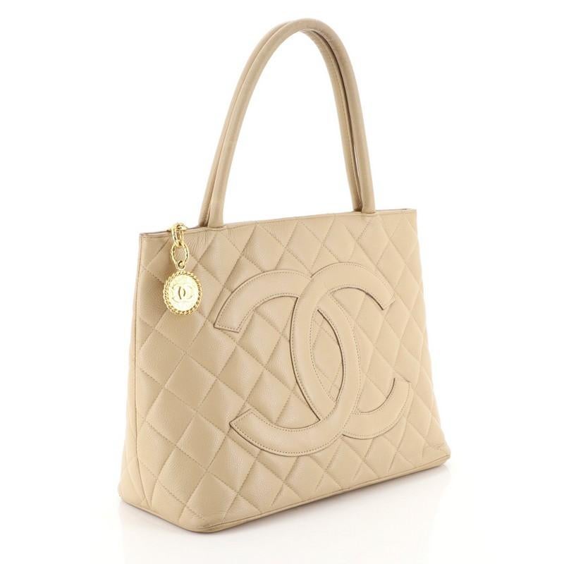 This Chanel Medallion Tote Quilted Caviar, crafted from neutral quilted caviar leather, features dual rolled tall handles, oversized stitched CC logo, and gold-tone hardware. Its zip closure opens to a neutral leather interior with slip and zip