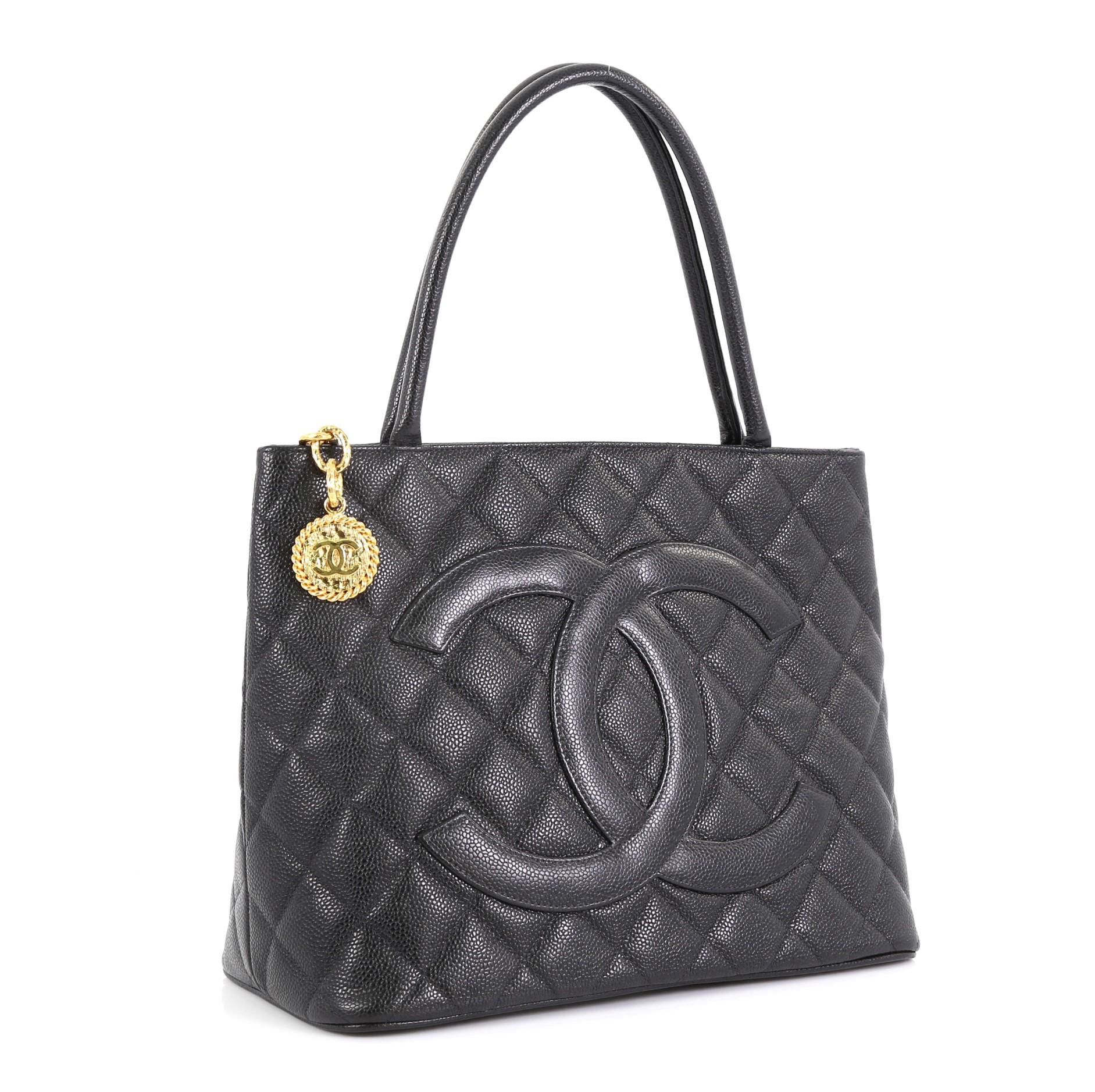 This Chanel Medallion Tote Quilted Caviar, crafted from black quilted caviar leather, features dual rolled tall handles, oversized stitched CC logo, and gold-tone hardware. Its zip closure opens to a black leather interior with slip and zip pockets.