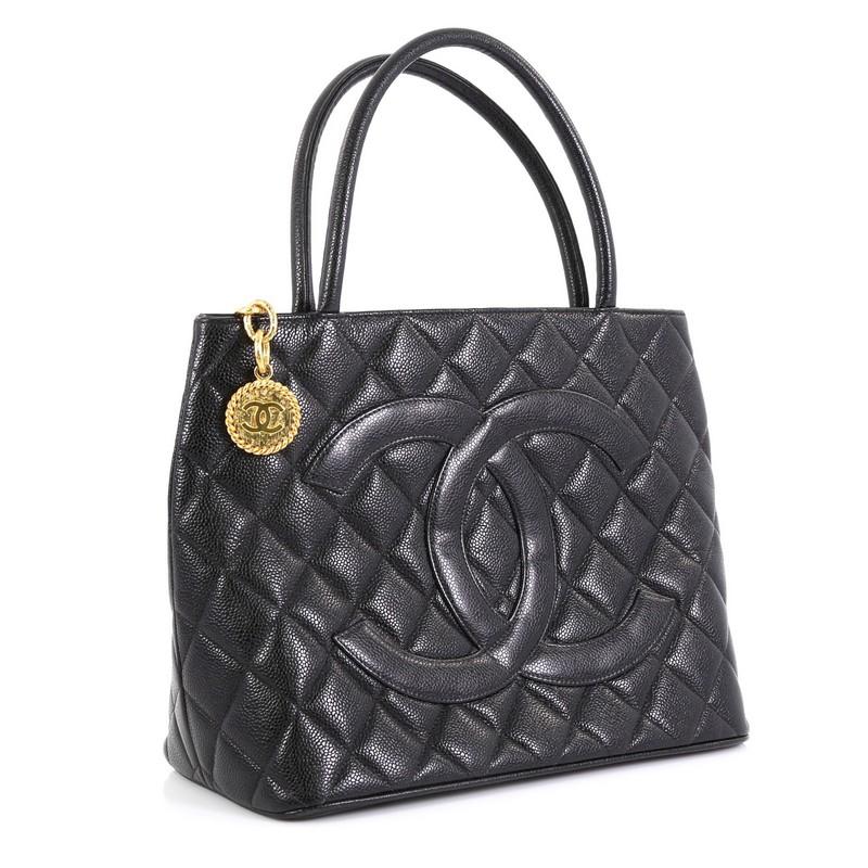 This Chanel Medallion Tote Quilted Caviar, crafted from black quilted caviar leather, features dual rolled tall handles, oversized stitched CC logo, exterior back slip pocket, and gold-tone hardware. Its zip closure opens to a black leather interior