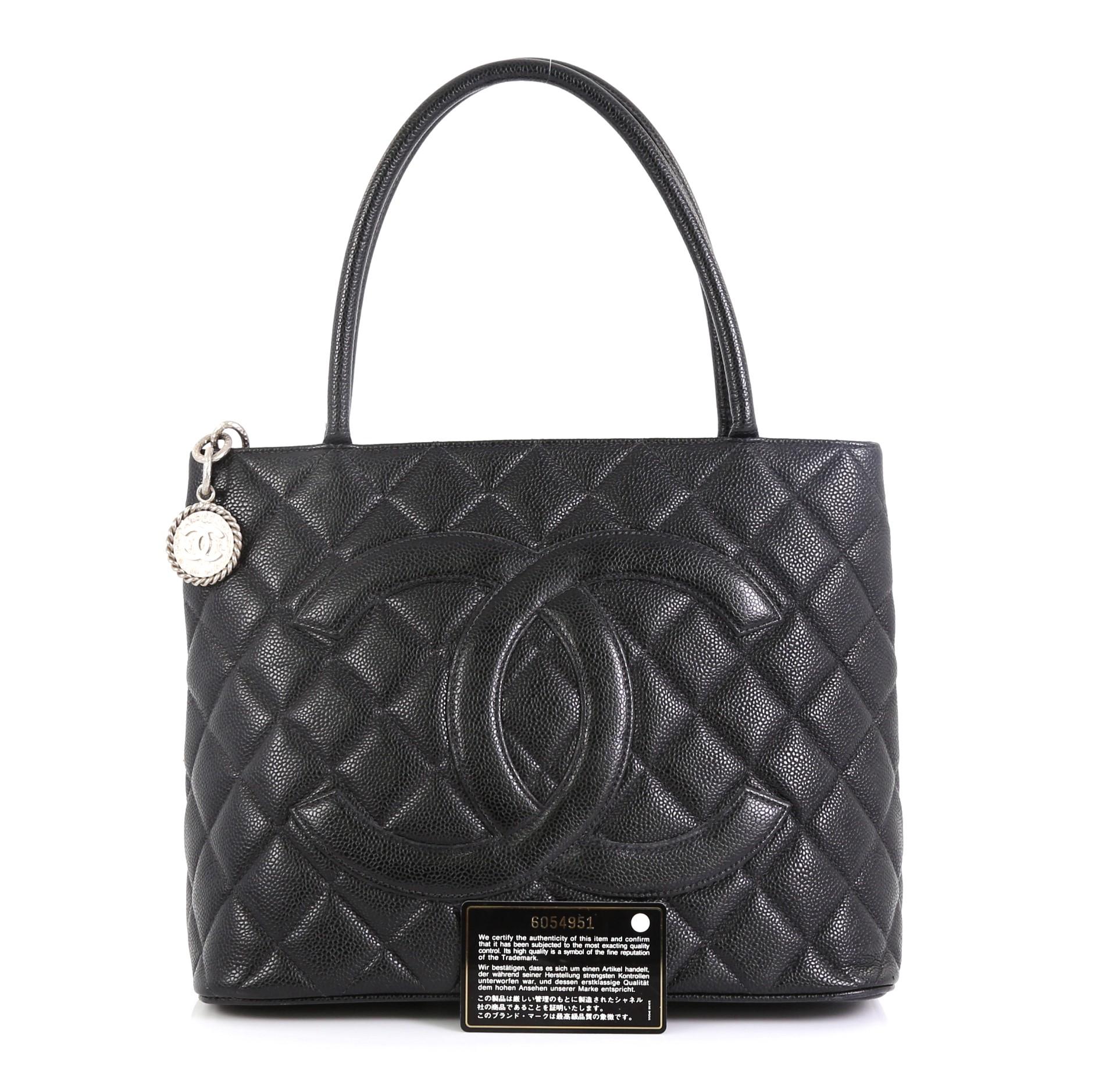 This Chanel Medallion Tote Quilted Caviar, crafted from black quilted caviar leather, features dual rolled tall handles, oversized stitched CC logo, and matte silver-tone hardware. Its zip closure opens to a black leather interior with slip and zip