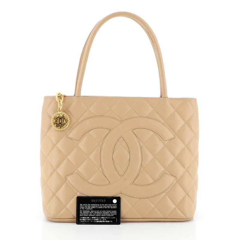 This Chanel Medallion Tote Quilted Caviar, crafted from neutral quilted caviar leather, features dual rolled tall handles, oversized stitched CC logo, exterior back slip pocket, and gold-tone hardware. Its zip closure opens to a neutral leather