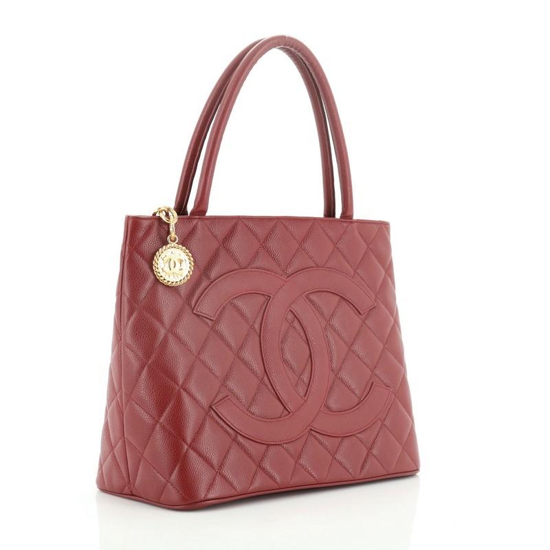 This Chanel Medallion Tote Quilted Caviar, crafted from red quilted caviar leather, features dual rolled tall handles, oversized stitched CC logo, exterior back slip pocket, and gold-tone hardware. Its zip closure opens to a red leather interior