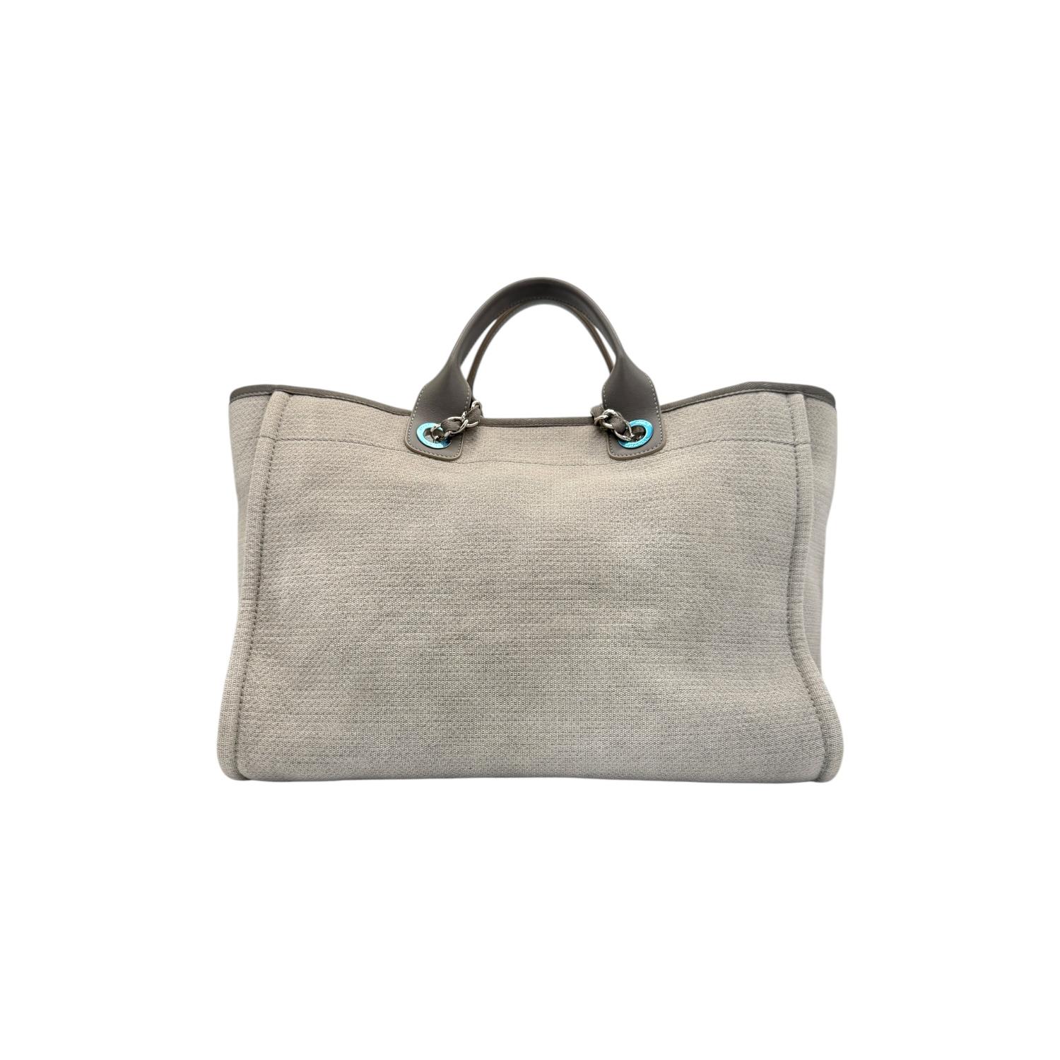 Entdecken Sie den Luxus und die Eleganz der Chanel Medium Grey Deauville Shopping Tote. Diese Designertasche aus strapazierfähigem Canvas mit silberfarbenen Beschlägen ist ein Highlight, das Stil mit Funktionalität verbindet. Mit geräumigen