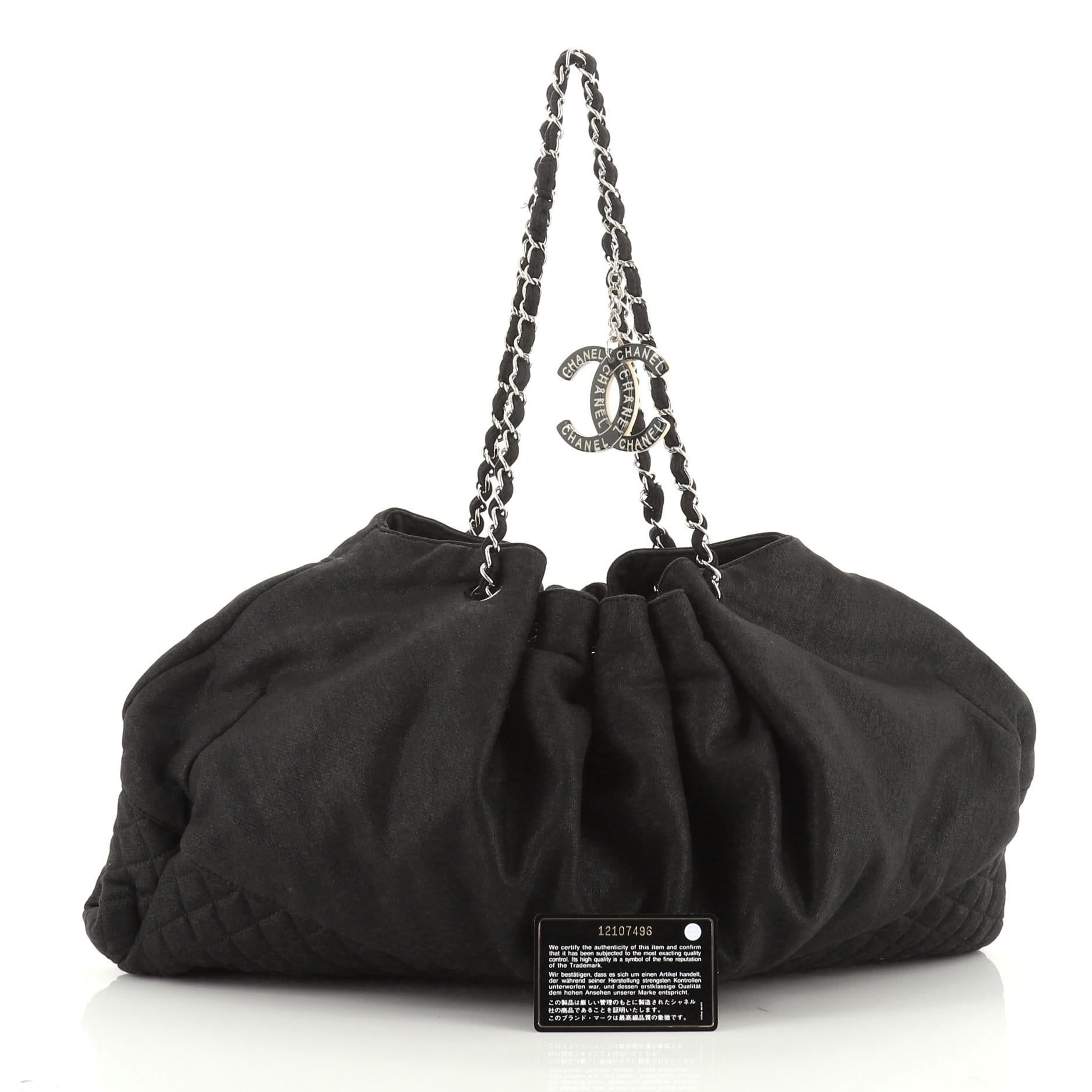 This Chanel Melrose Cabas Tote Jersey Medium, crafted from black jersey, features quilted diamond base, woven-in leather chain strap, and silver-tone hardware. Its drawstring closure opens to a gray silk interior with slip pockets. Hologram sticker