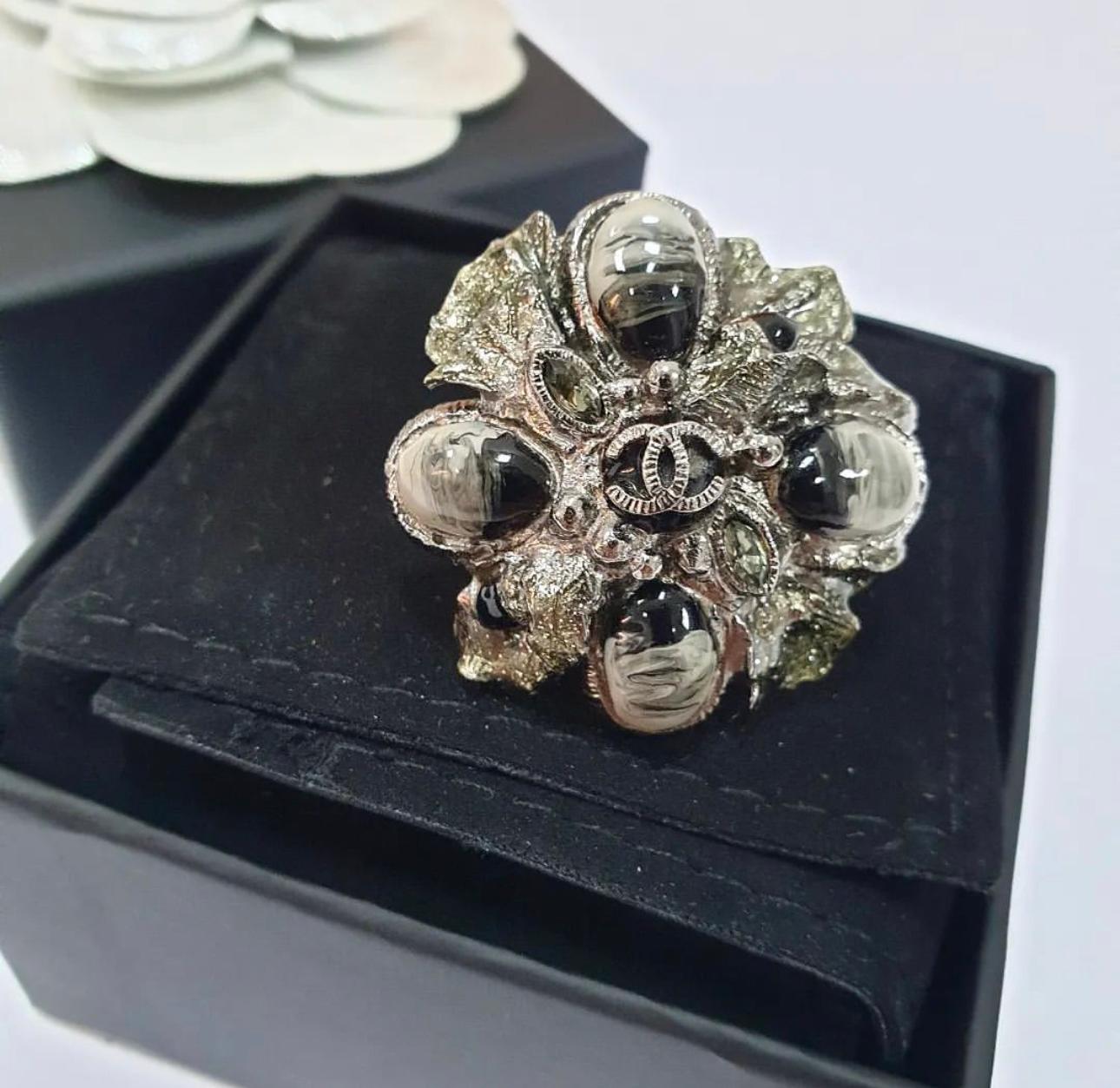 This fabulous ring features gunmetal colored metal with a small CC logo in the center and a painted enamel flower design. 
A fabulous accessory for any Chanel lover!

Size 17-17.5

100% AUTHENTIC

Comes with box.